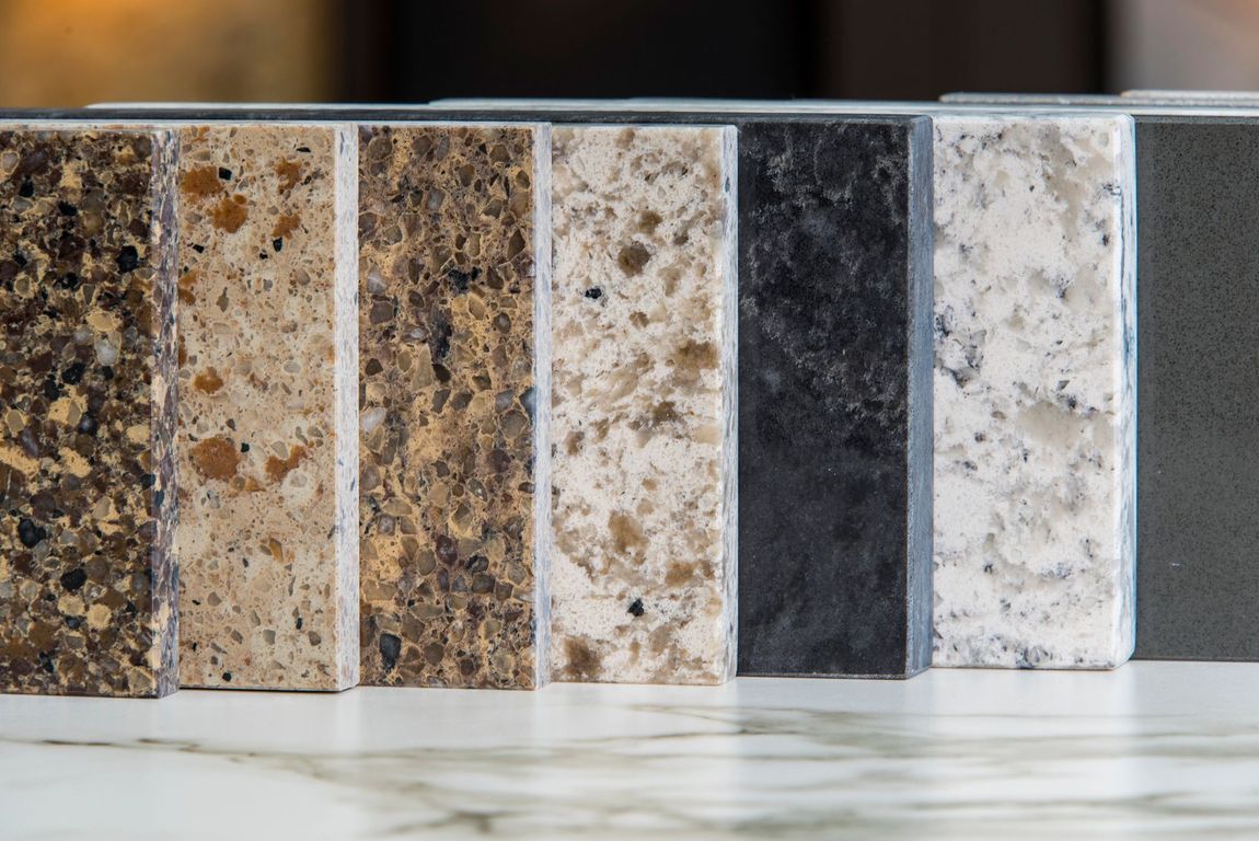 Una fila di sette campioni verticali di piani di lavoro in pietra che mostrano vari colori e texture, dal marrone scuro al bianco.