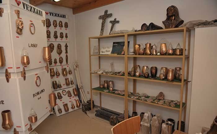 Scaffali espositivi in ​​uno showroom con varie urne funerarie in bronzo, targhe commemorative e croci religiose.