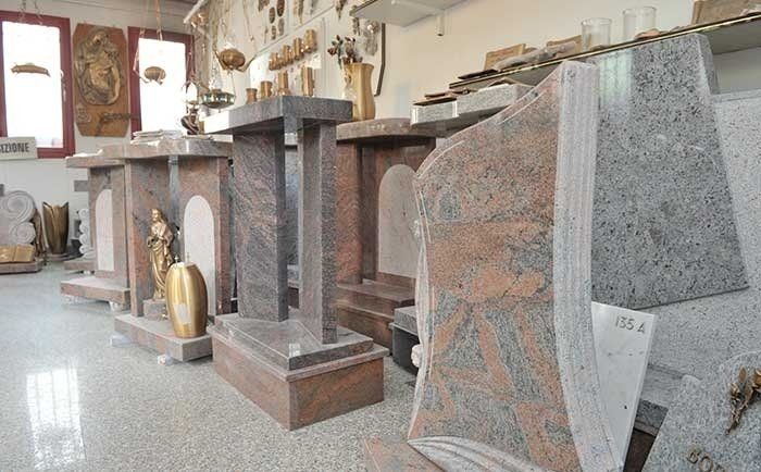 Uno showroom che espone diverse lapidi in granito e marmo, tra cui monumenti sagomati e piccole urne.