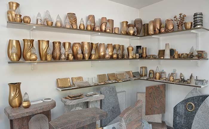 Una sala espositiva con scaffali pieni di varie urne dorate, vasi e monumenti commemorativi in ​​pietra.