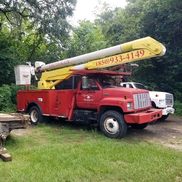 Red bucket truck with a raised yellow boom in a grassy area, a white truck in the background.