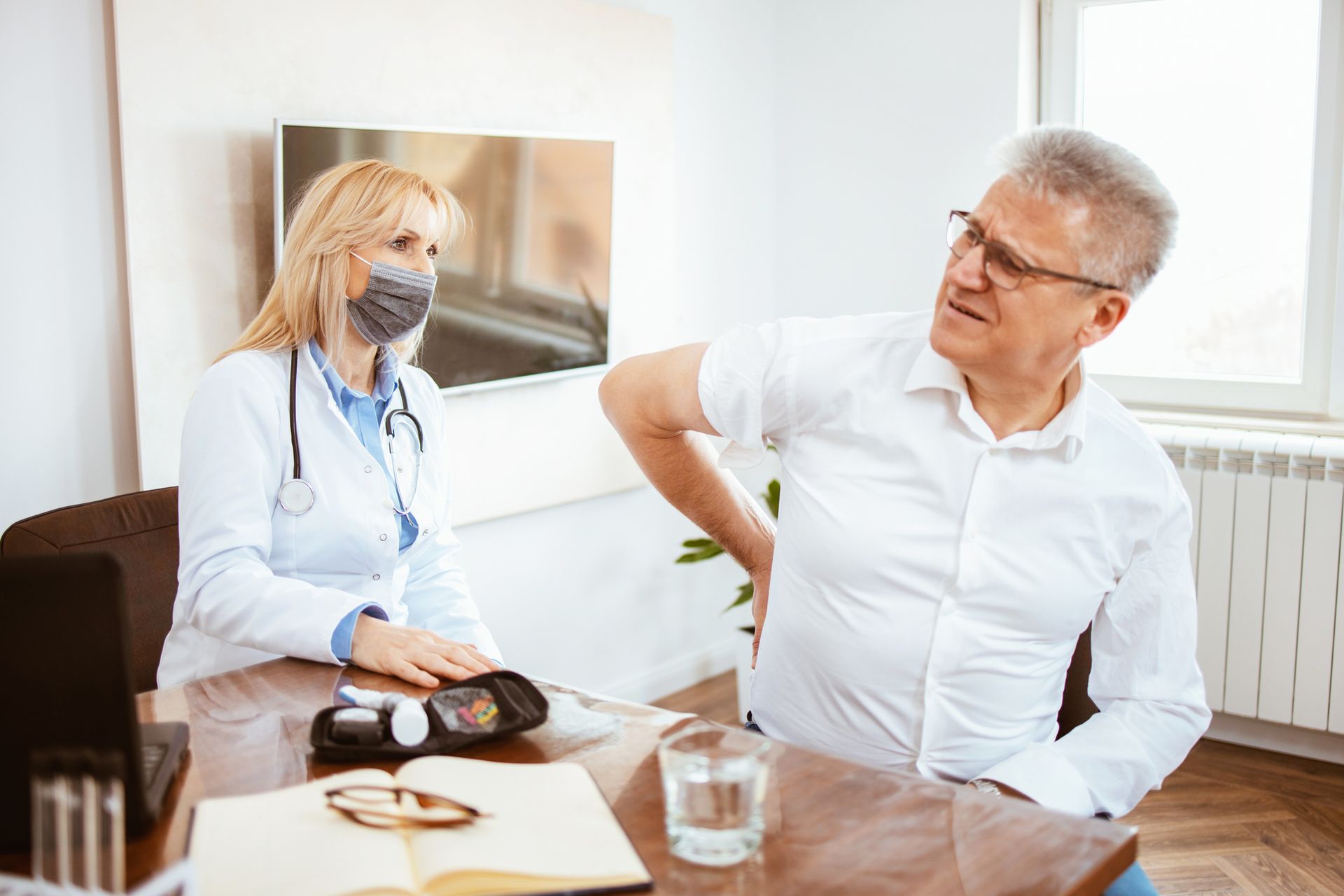 A man is sitting at a table talking to a doctor who is wearing a mask. A man is sitting at a table talking to a doctor who is wearing a mask.