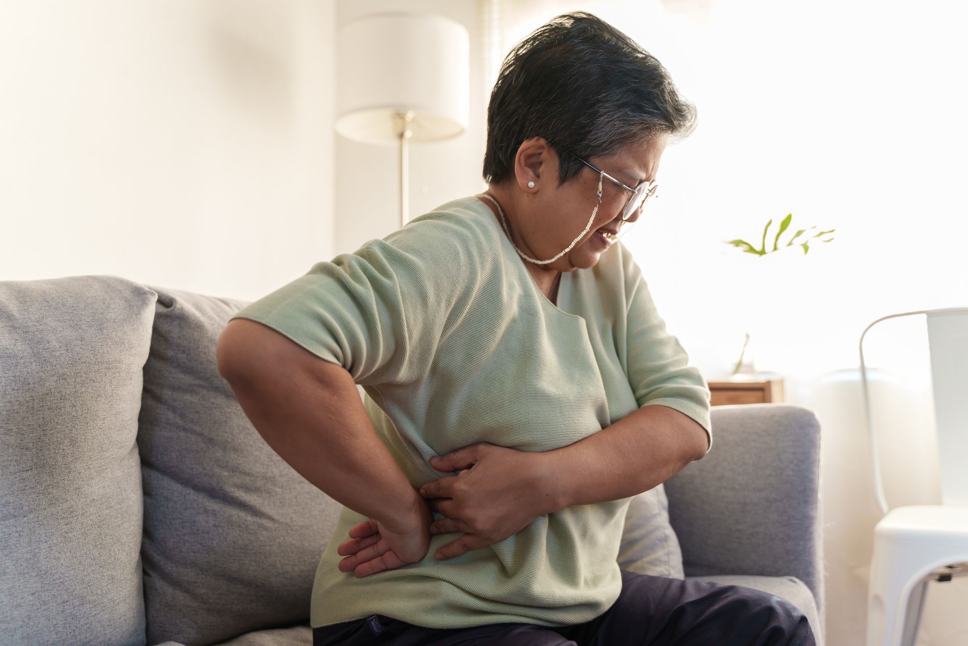 A Woman is Sitting on a Couch Holding her Back in Pain — Orlando, FL — Central Florida Kidney Specialists