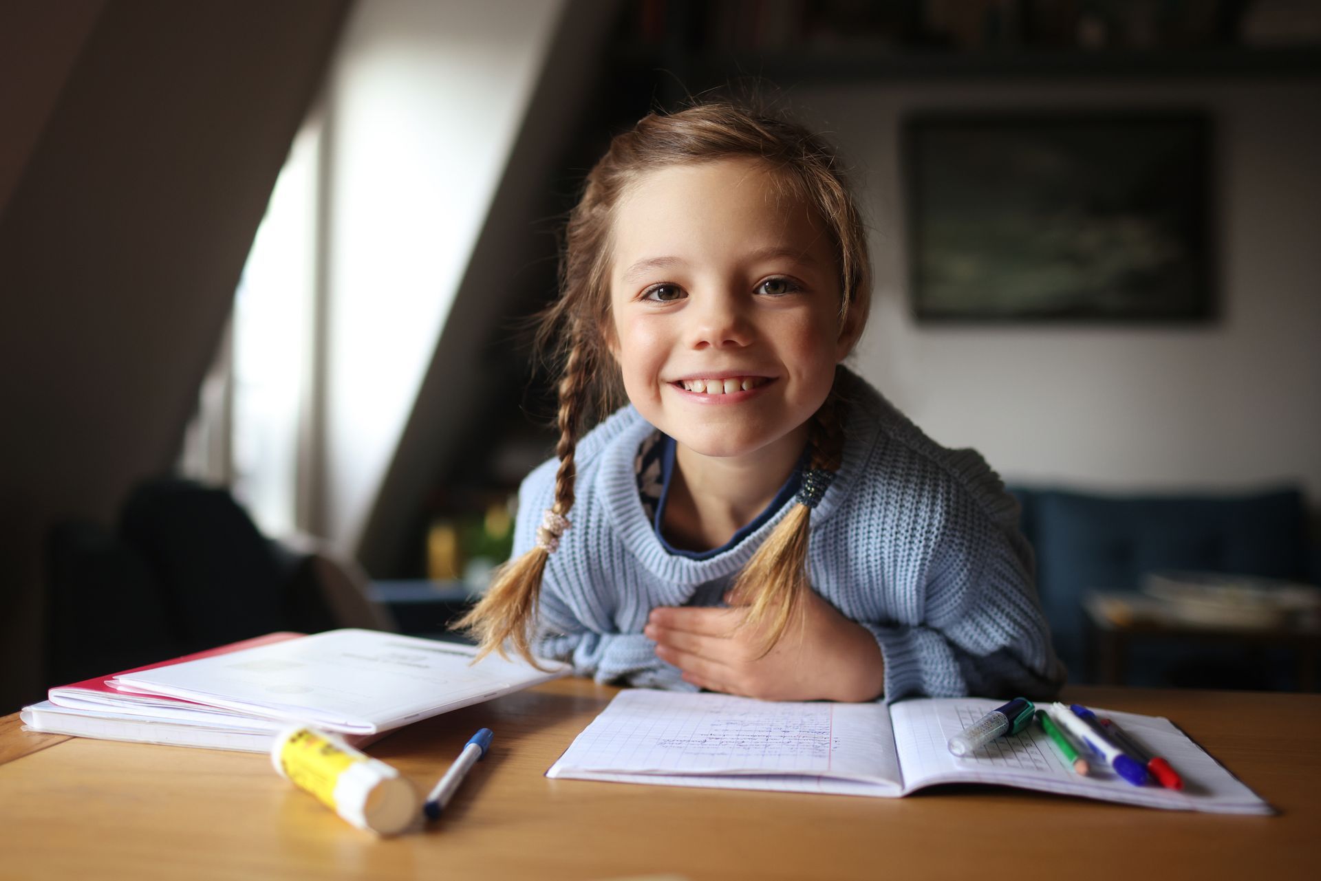 A little girl is sitting at a table with a notebook and markers.