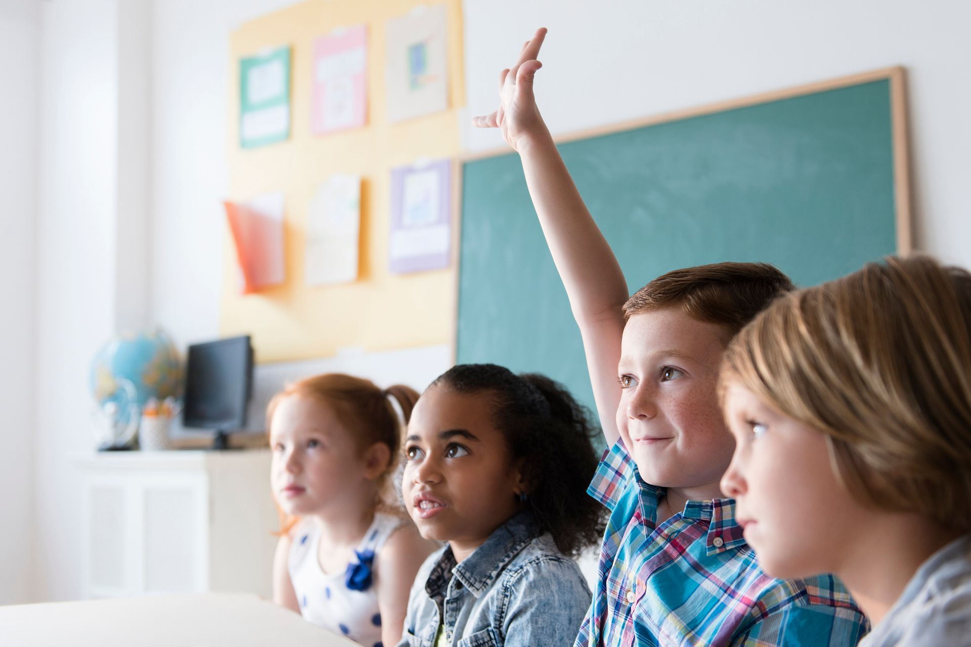 A group of children are raising their hands in a classroom to answer a question.