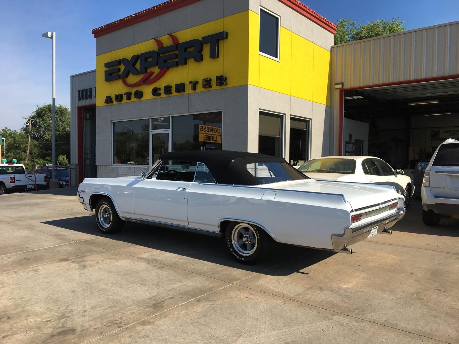 White classic convertible parked outside an auto service shop on a sunny day