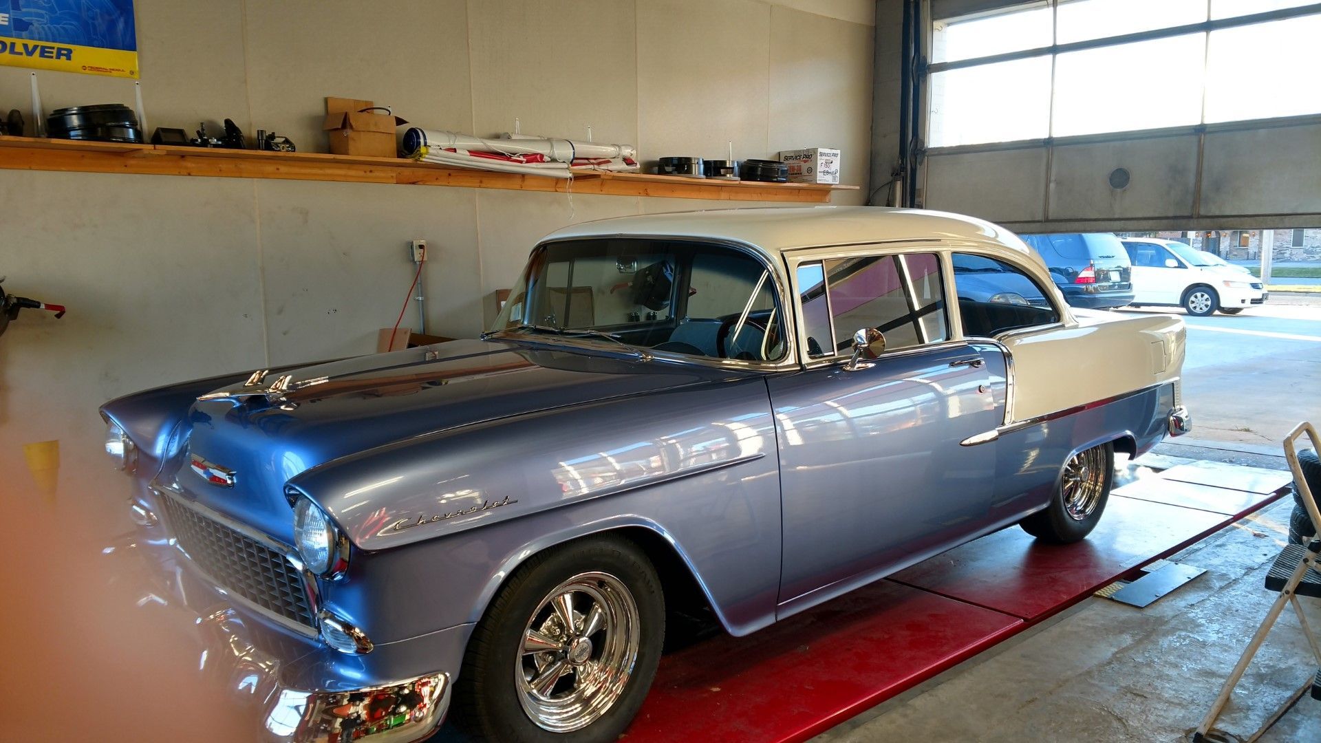 Classic blue vintage car on a lift in a garage, with shelves and another car visible in the background.