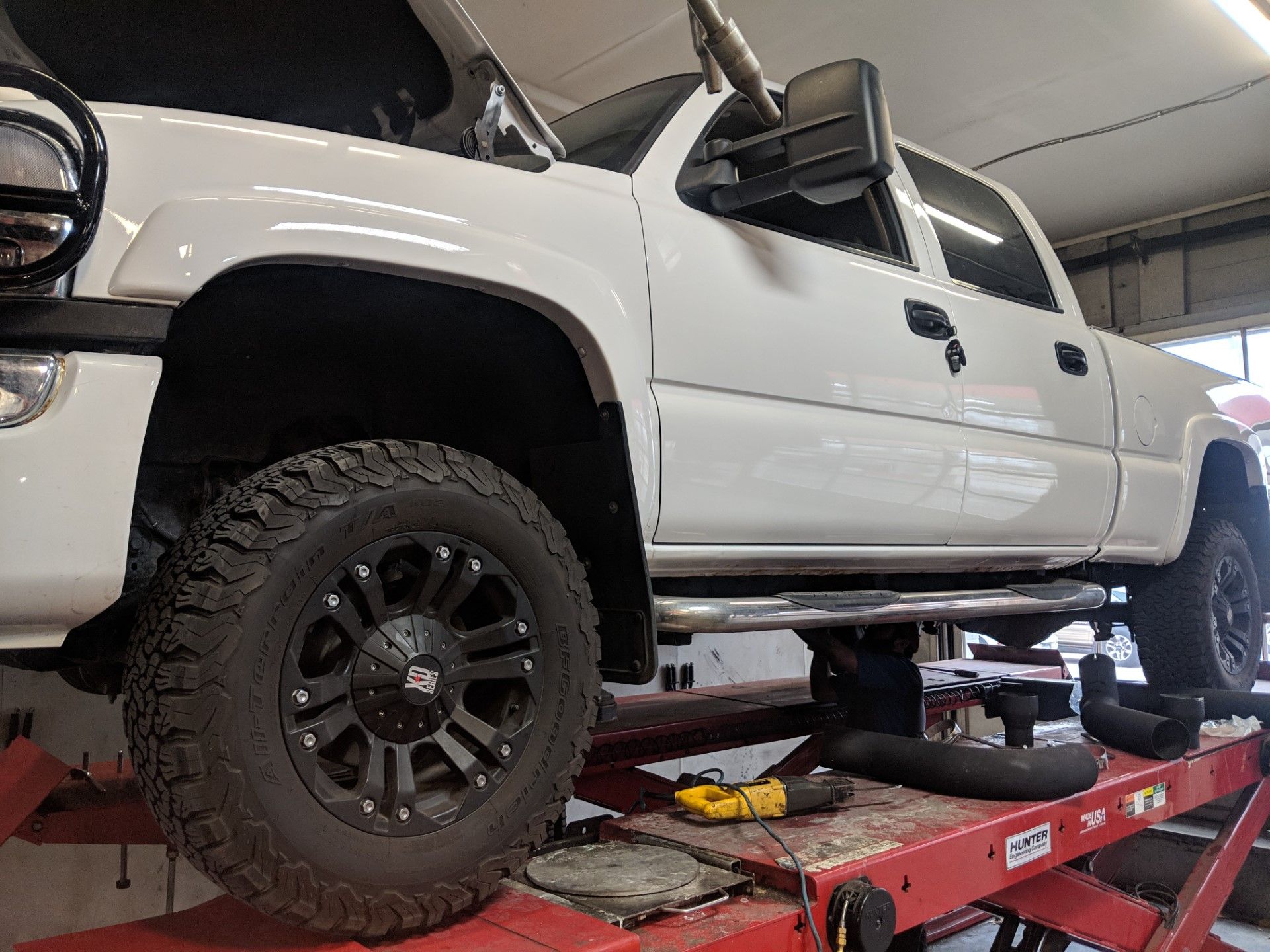 White lifted pickup truck on a red vehicle lift in a garage workshop.