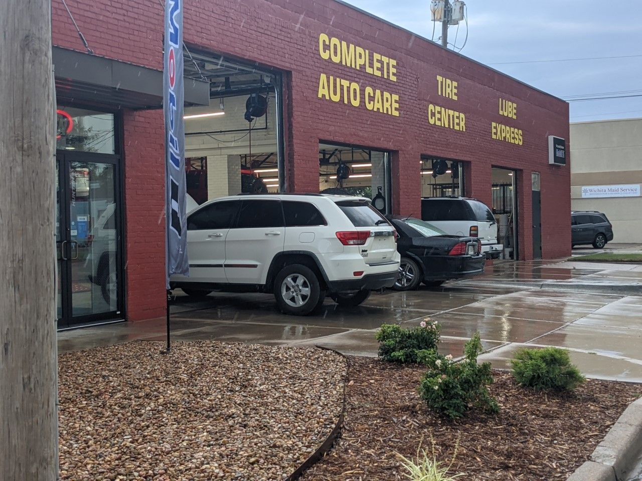 Auto repair shop with two SUVs parked outside in the rain; sign reads “Complete Tire and Auto Care.”