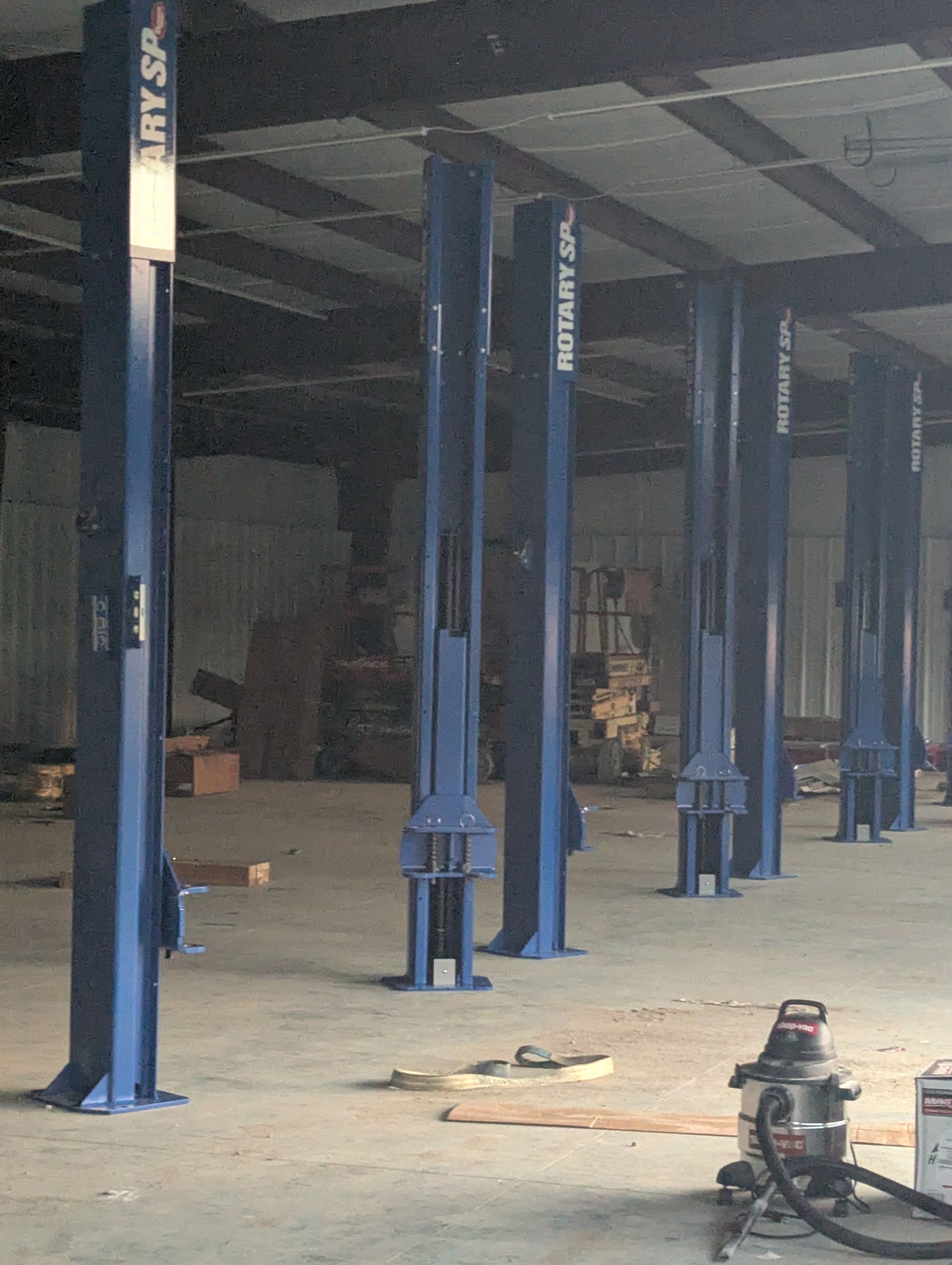Empty warehouse interior with blue steel support columns and a small machine on the floor.