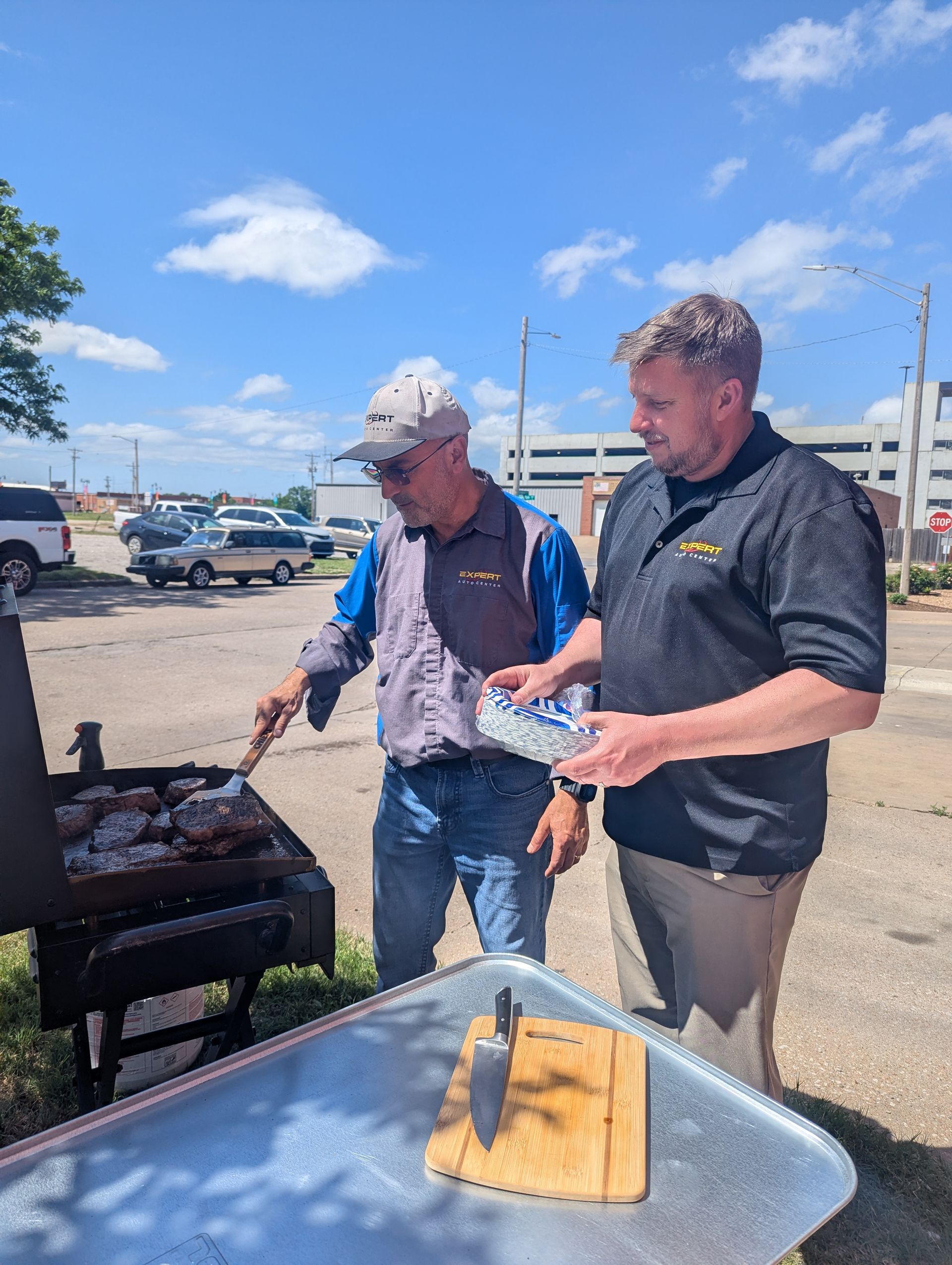 Two men grilling outdoors beside a tray with a fish fillet on a sunny day