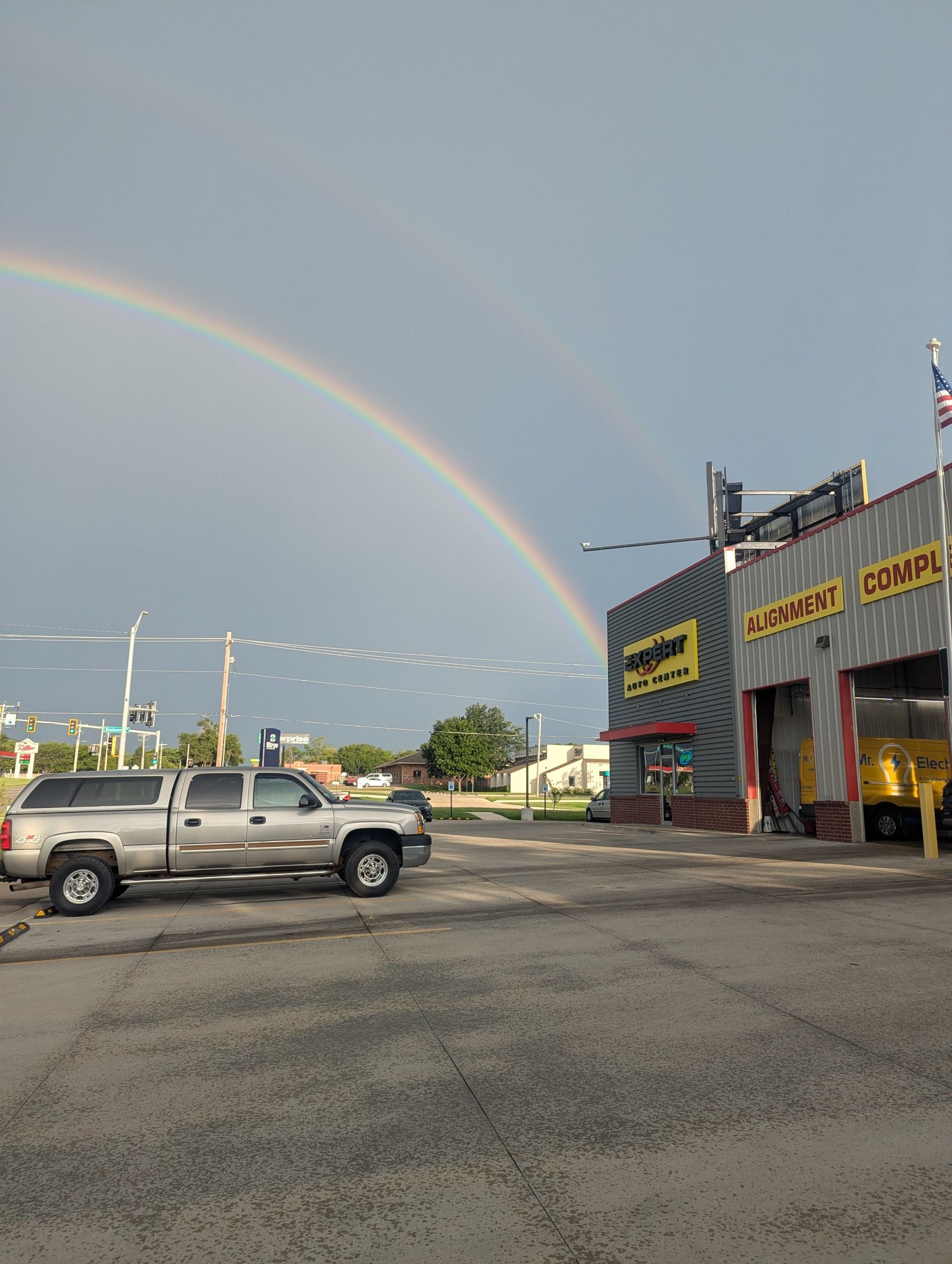 Rainbow over a parking lot beside a commercial building and pickup trucks at dusk