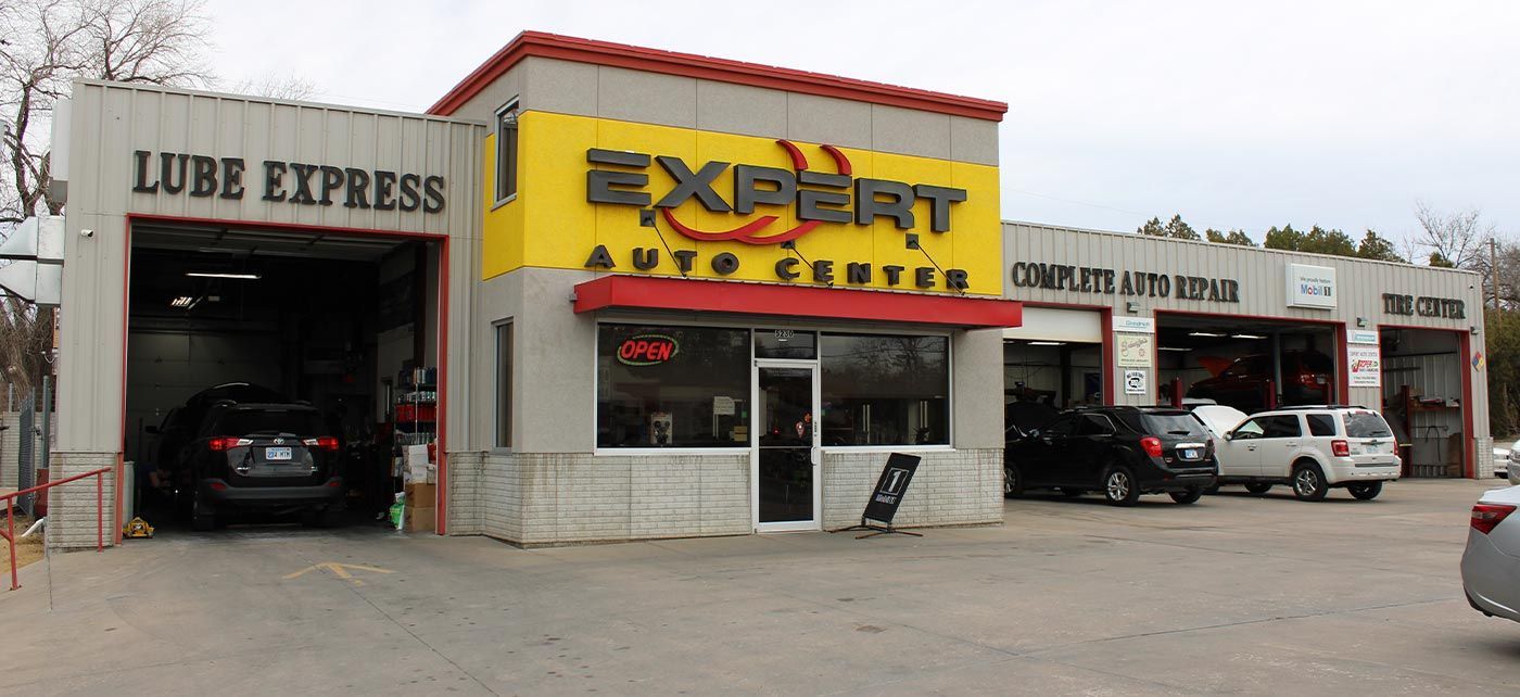 Auto repair shop storefront with yellow “Excel Auto” sign, open garage bays, and parked cars