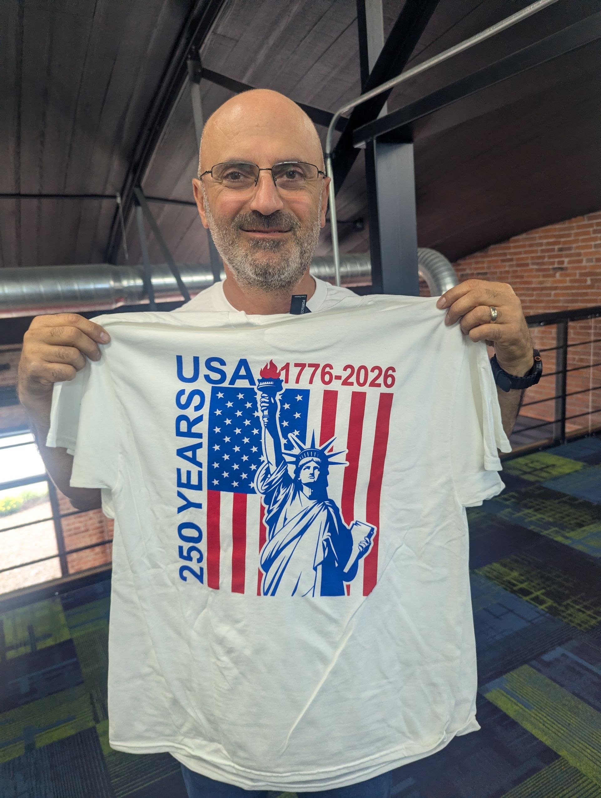 Man holding white USA 250 years 1776–2026 T-shirt with Statue of Liberty and American flag graphic