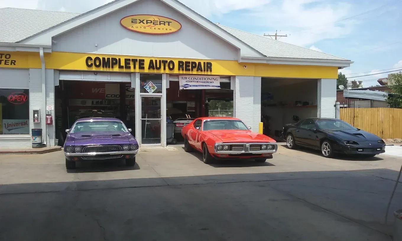 Auto repair shop storefront with three parked cars: purple, red, and black.