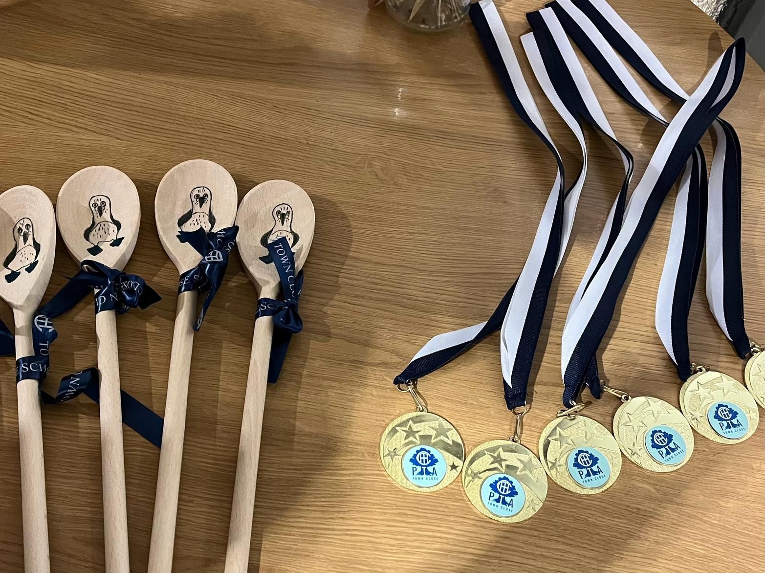 Wooden spoons painted with penguins, and gold medals with blue ribbons on a wooden table.