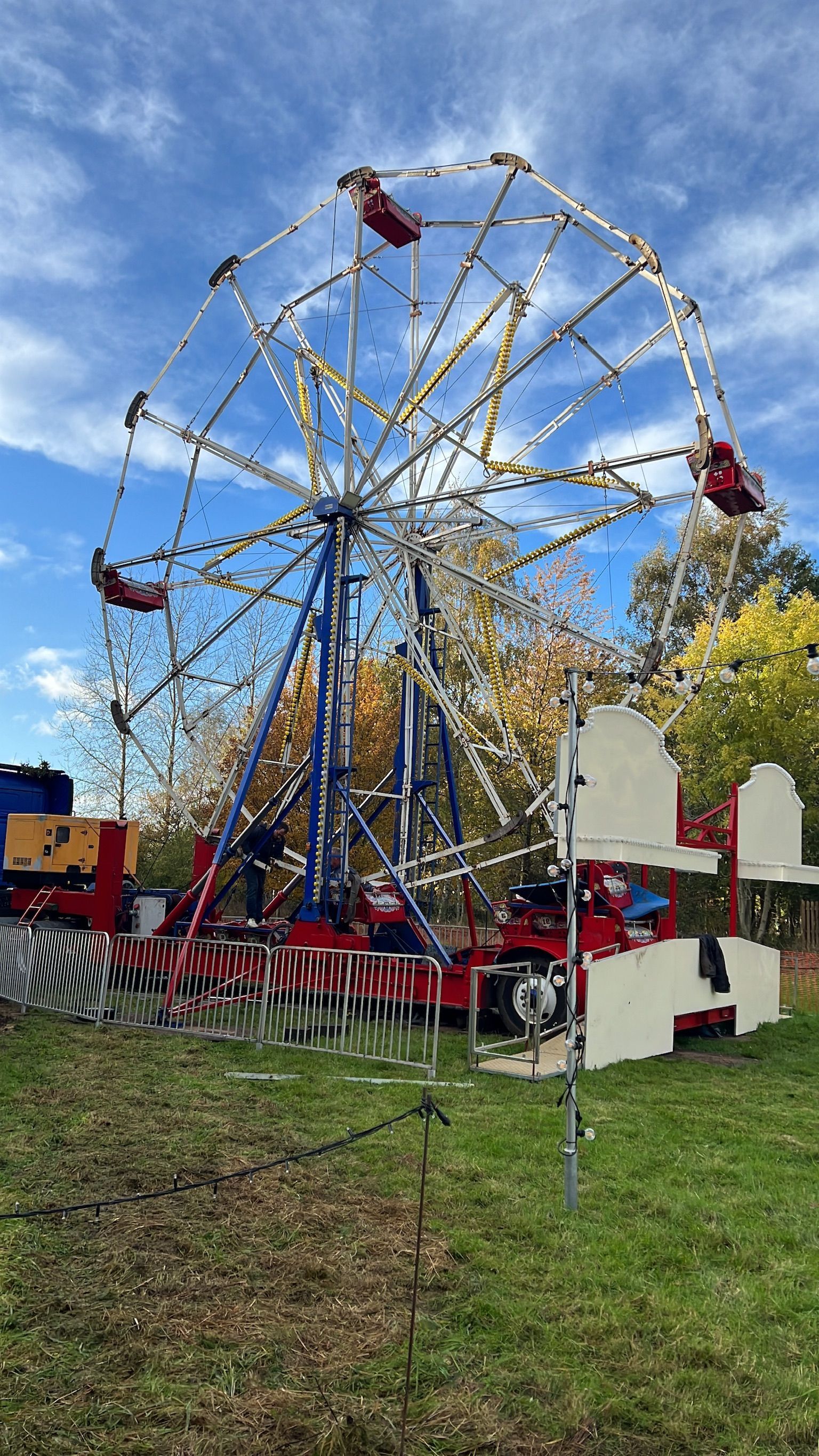 Ferris wheel at a fair, blue sky, red and white accents, grassy field.