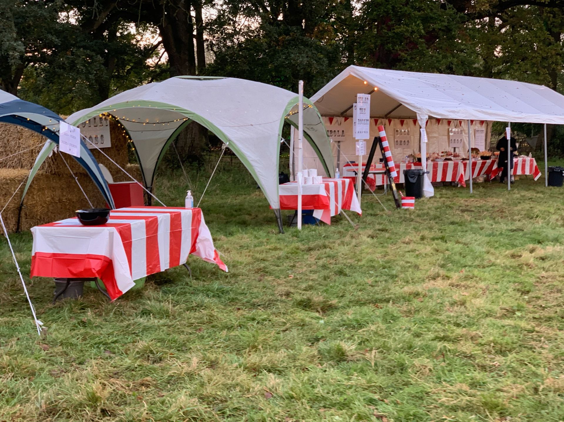 Outdoor event with white tents, red & white striped tables, and food.