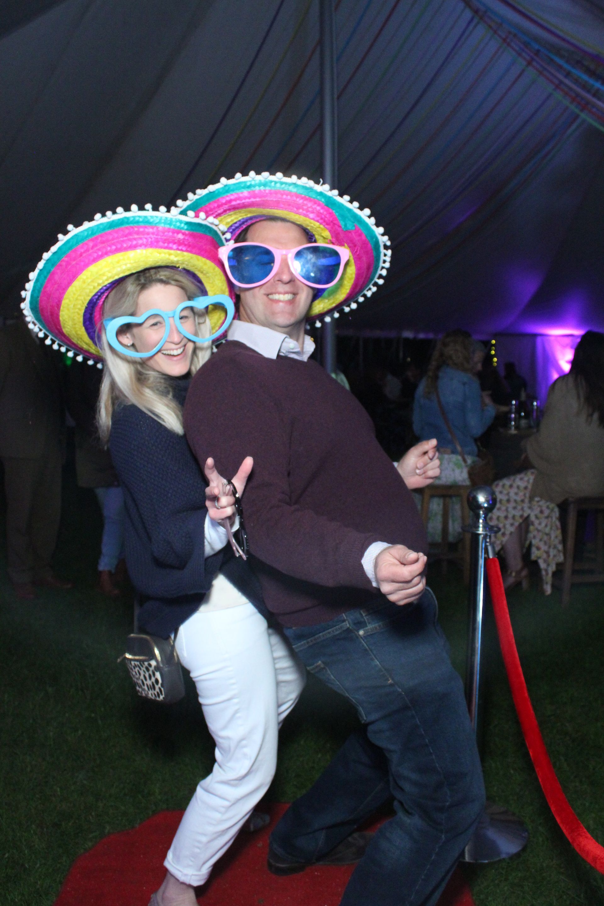 Couple in photo booth, wearing novelty glasses and sombreros, posing and smiling.