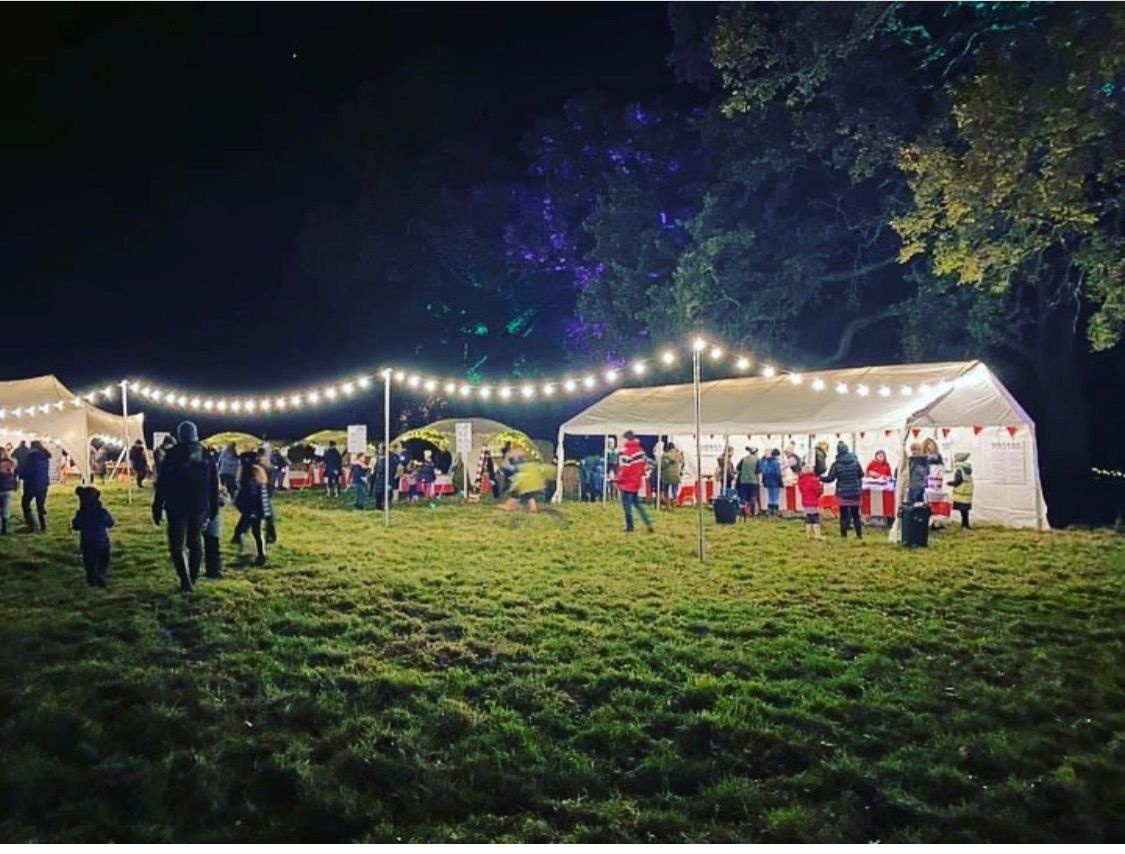 Night scene: outdoor event with tents, string lights, and people on a grassy field.