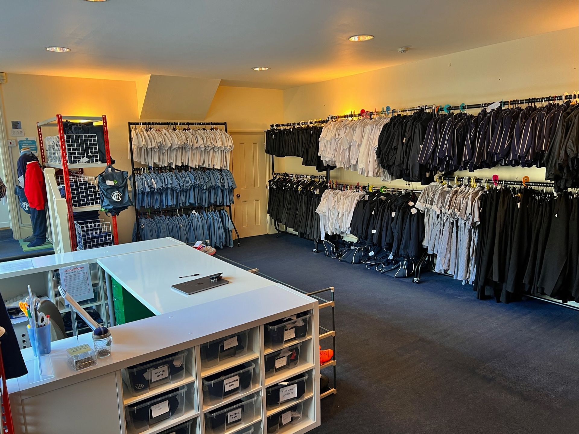 Clothing store interior with clothing racks displaying black and white garments, a checkout counter, and blue carpet.