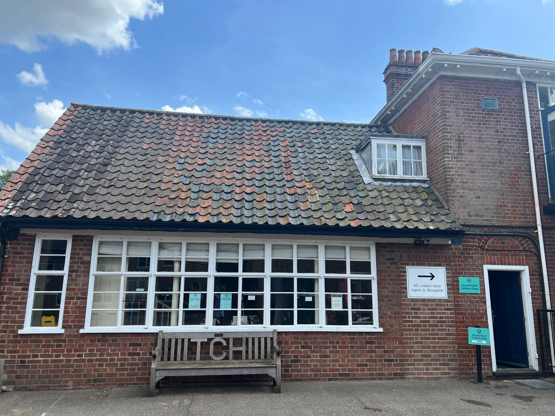 Red brick building with white-framed windows and a bench. Sign reads