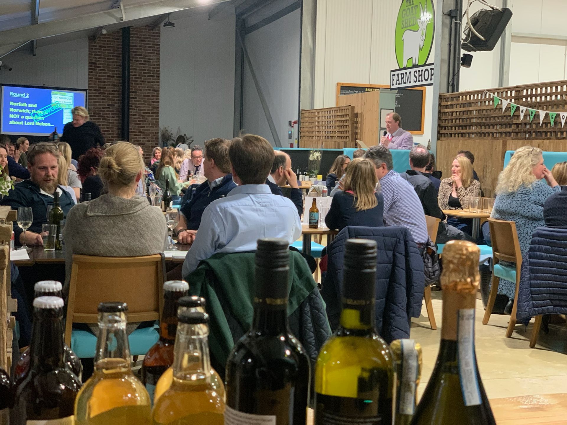People attending an event at a brewery, seated at tables. Bottles of beverages are in the foreground.