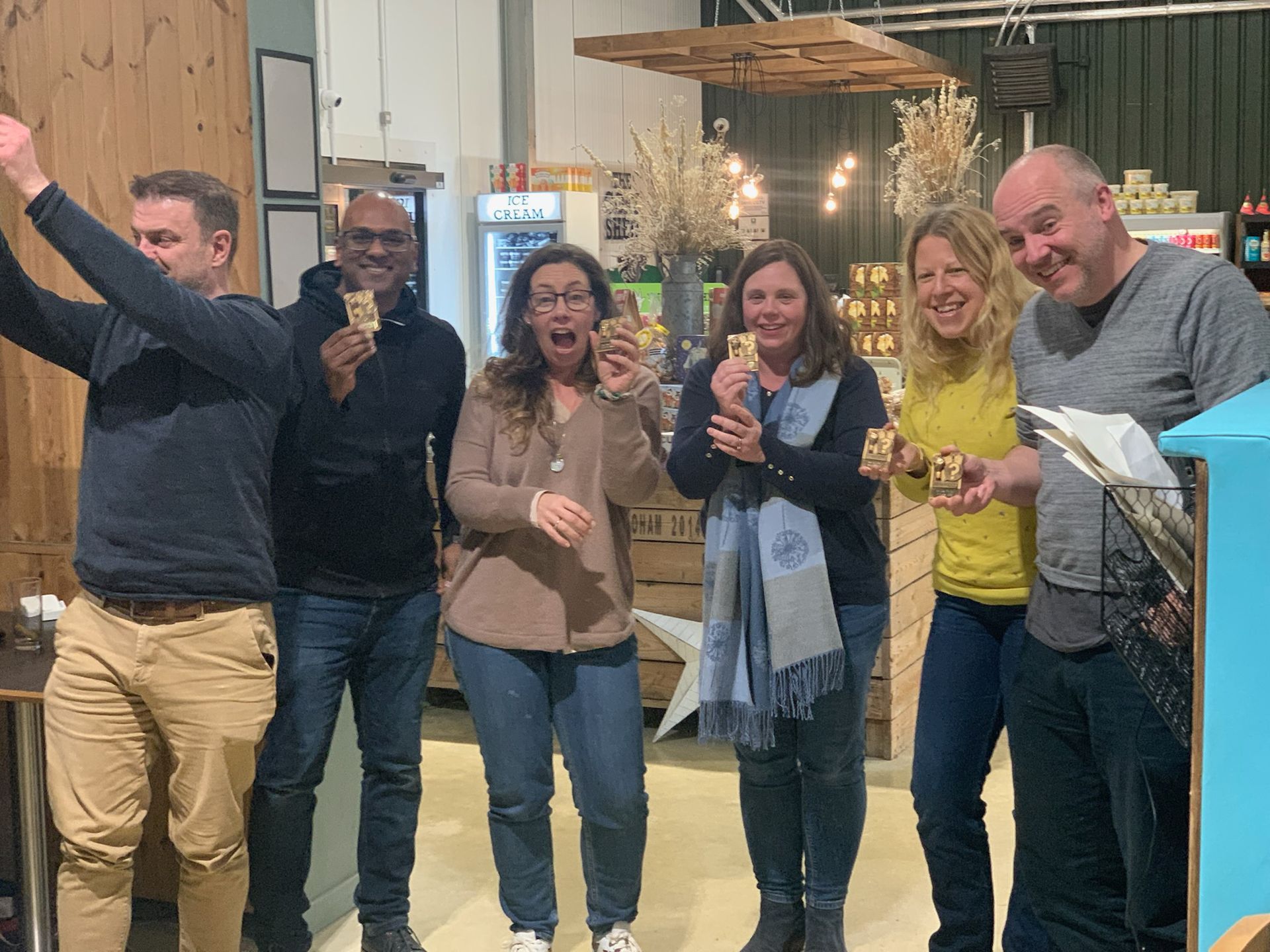 Group of six people inside a store, all smiling and eating. One person has arms raised in celebration.