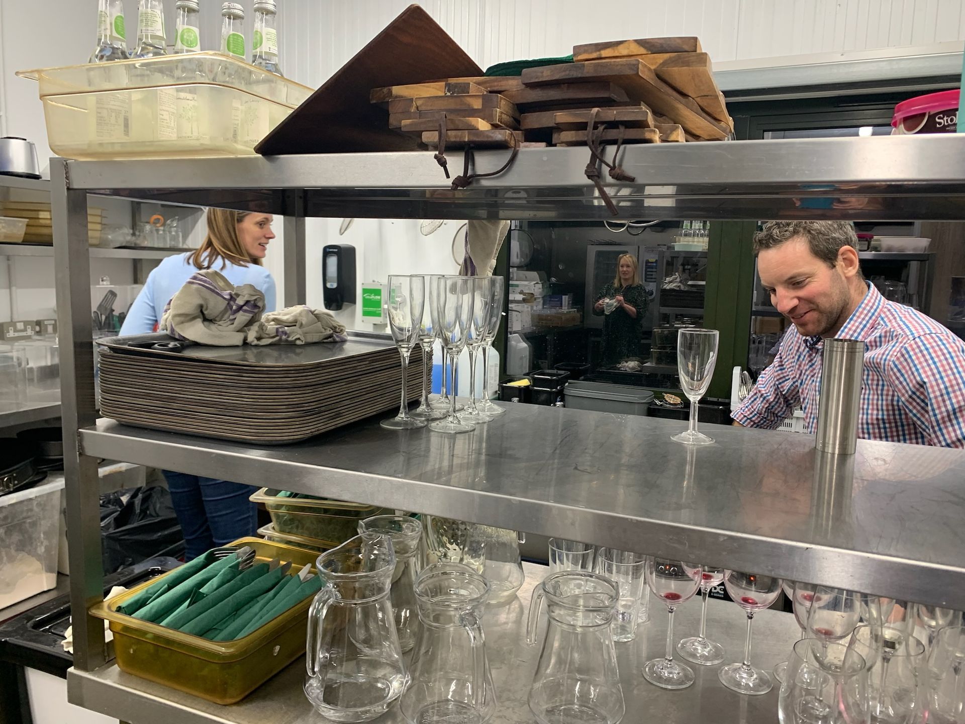 Two people working in a restaurant kitchen. One prepares a drink; the other cleans. Stainless steel shelves.