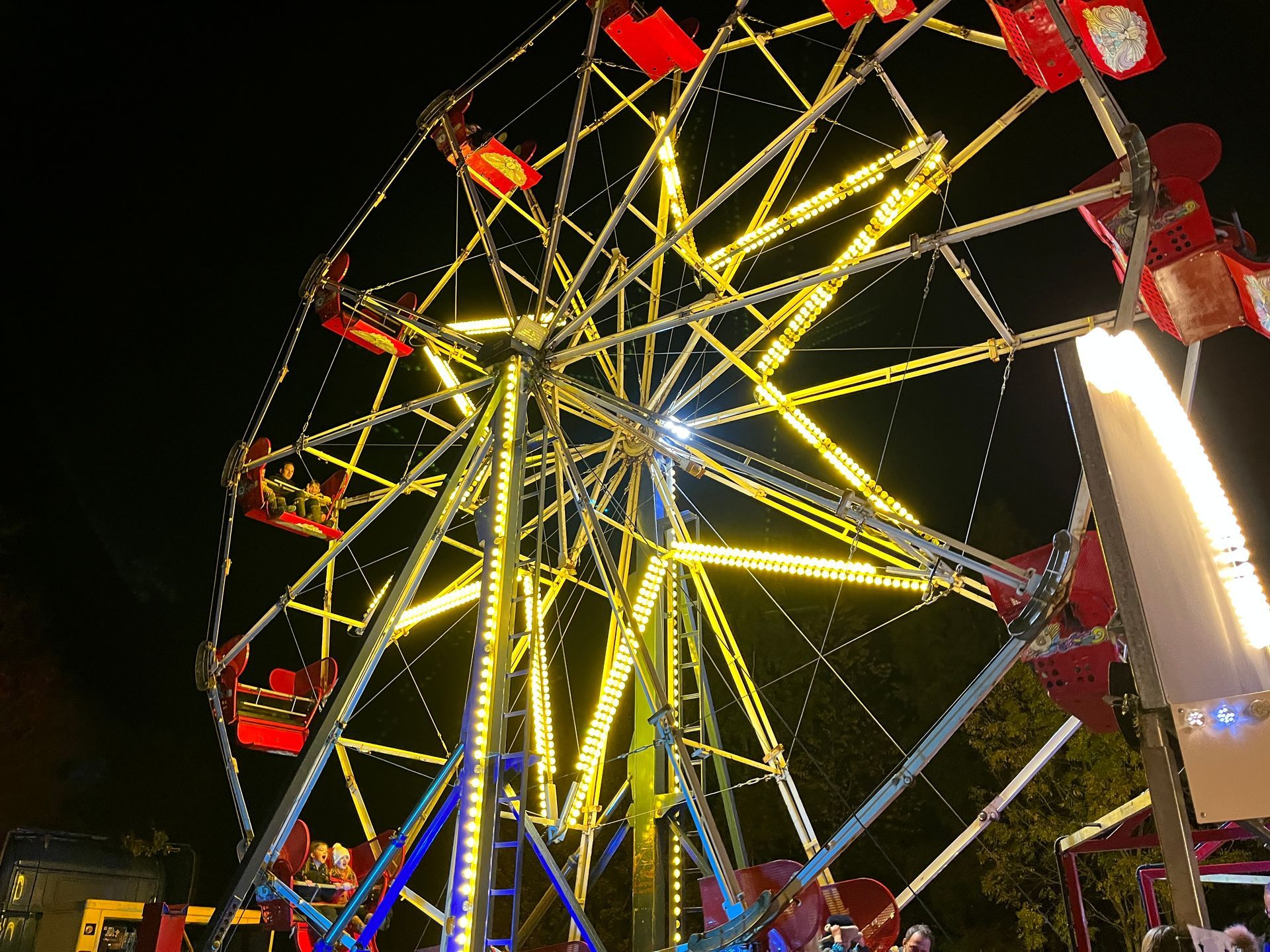 Ferris wheel at night, illuminated with yellow lights against a dark sky. Red gondolas.