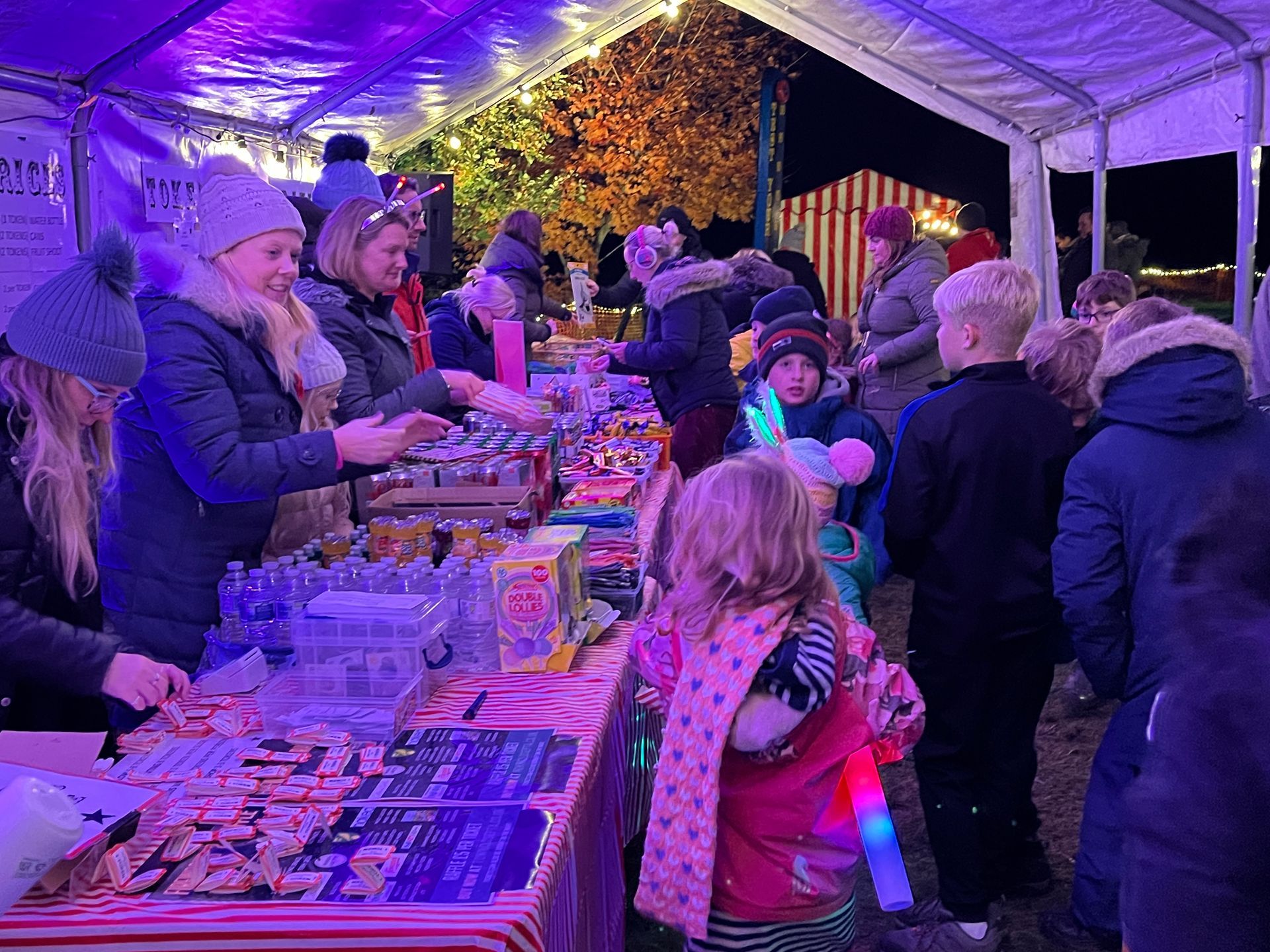 People at a brightly lit outdoor market stall selling candy and treats.