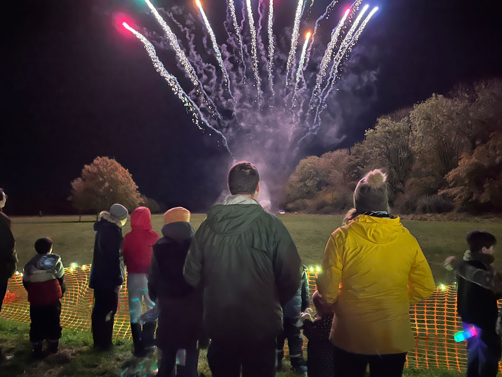 People watch fireworks erupt over a field at night.