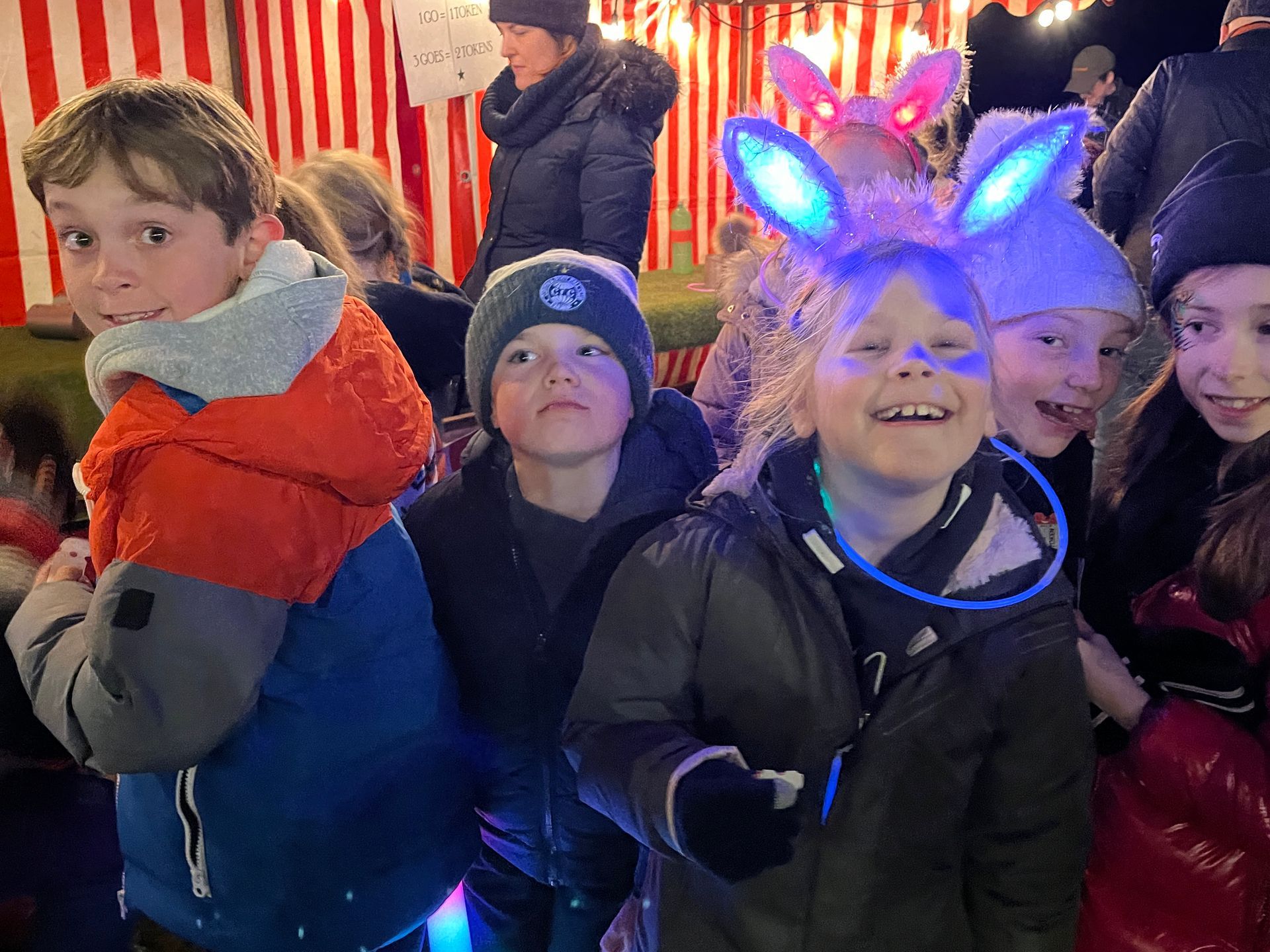 Group of kids smiling outdoors, some wearing glow-in-the-dark accessories, at night.