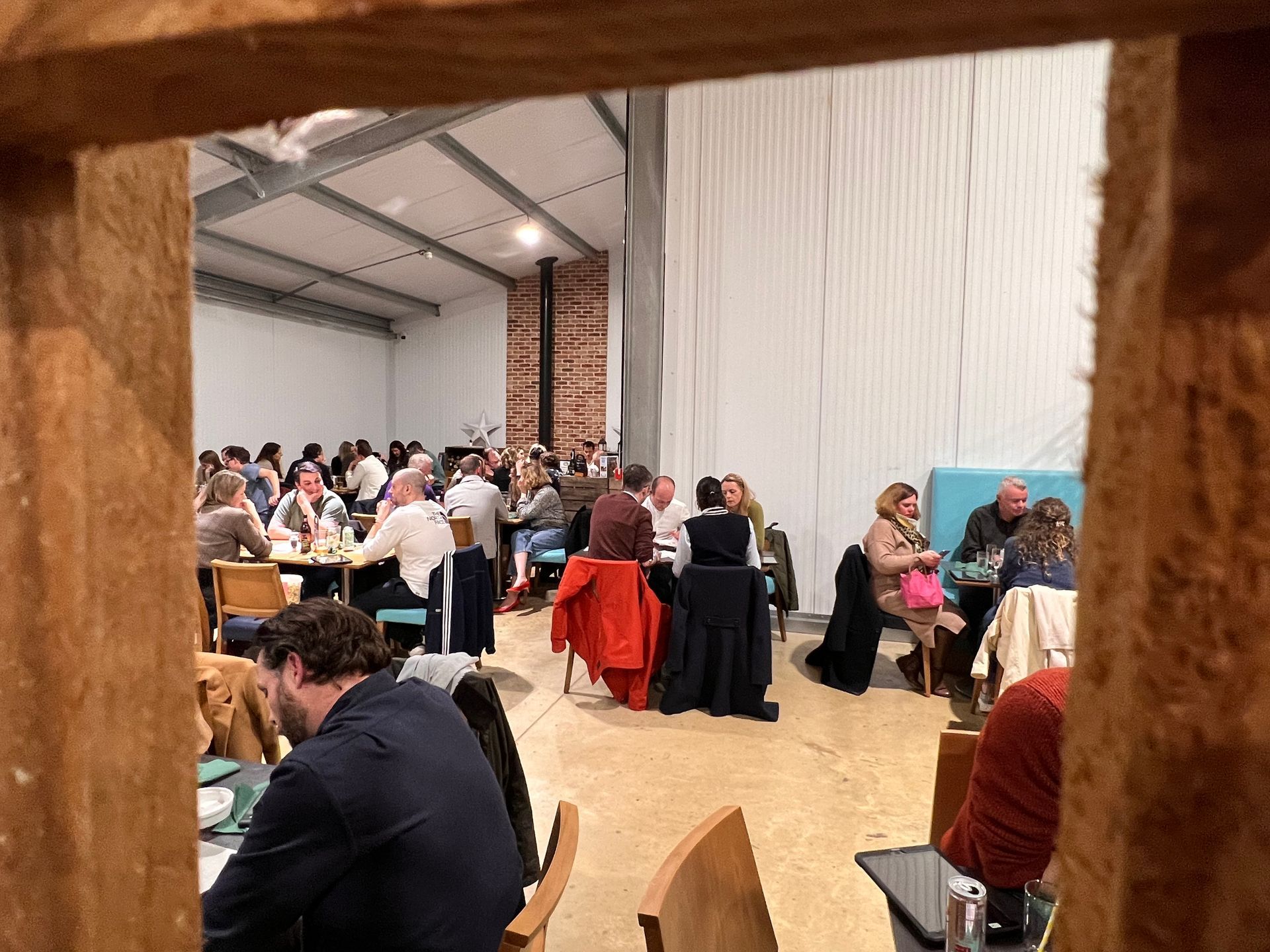 People seated at tables in a large hall, viewed through a wooden frame; likely a social event.