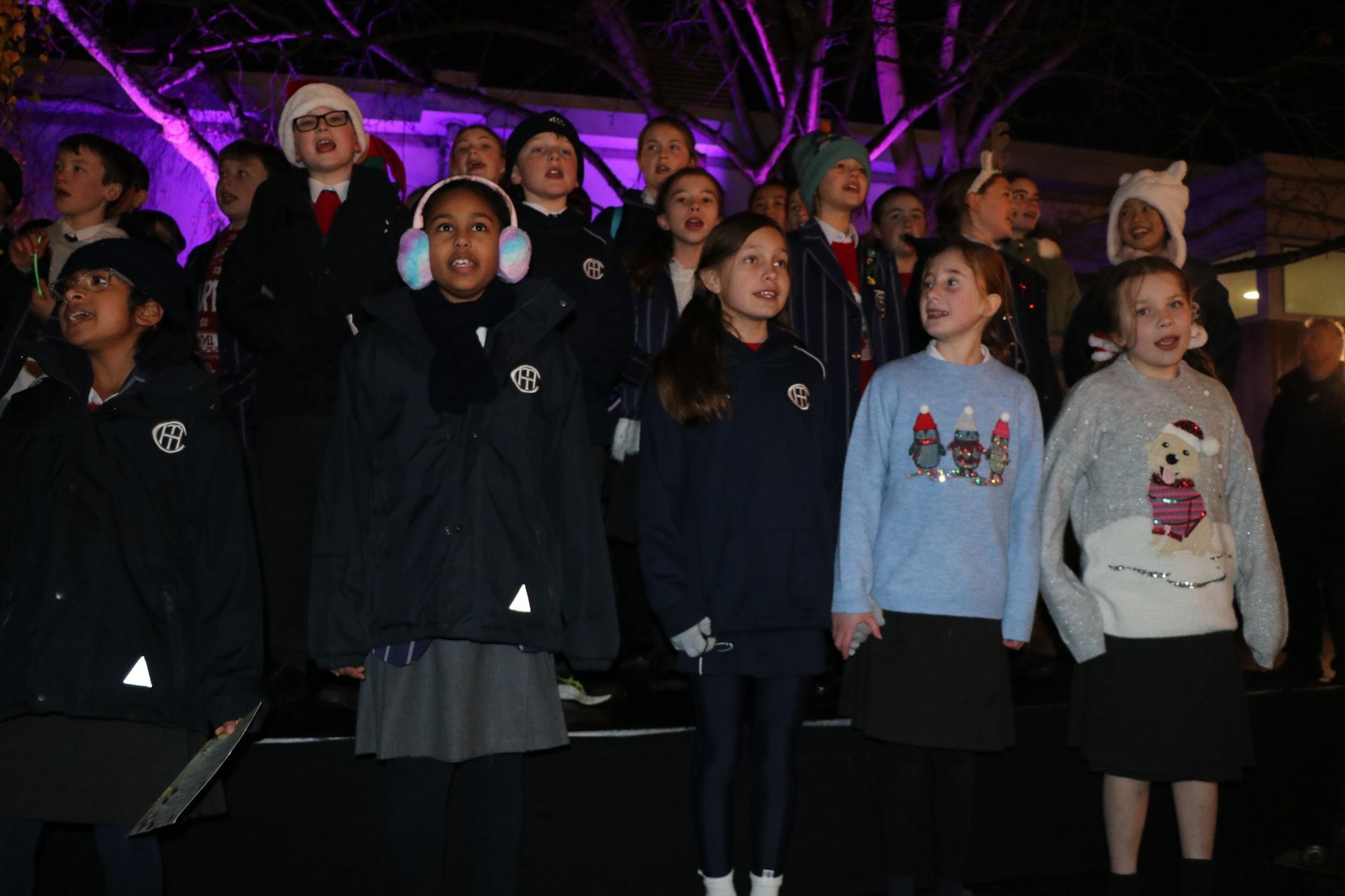 Children in winter clothes singing outdoors at night.