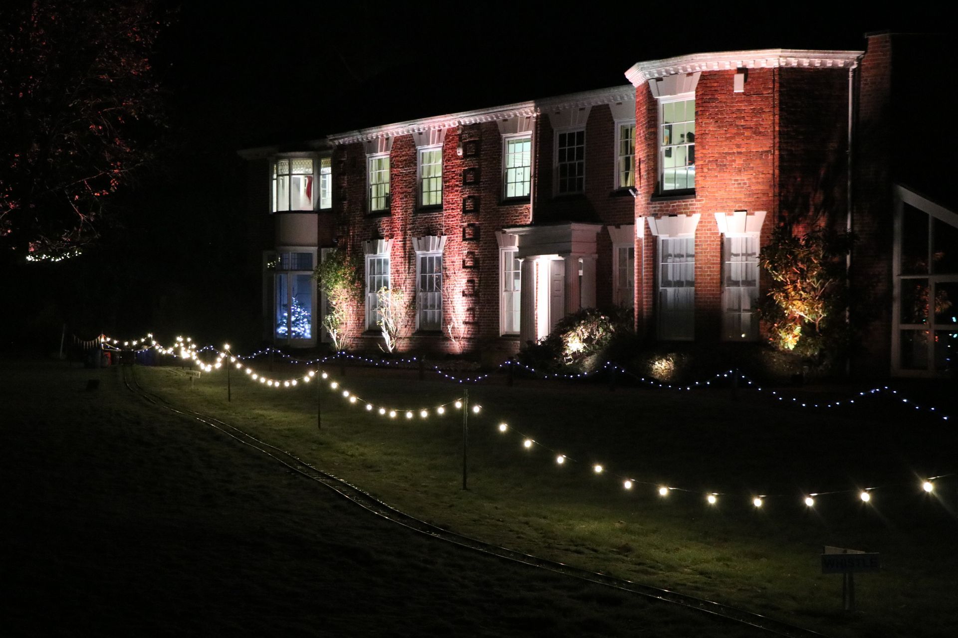 A two-story brick house illuminated at night with string lights leading up to it.