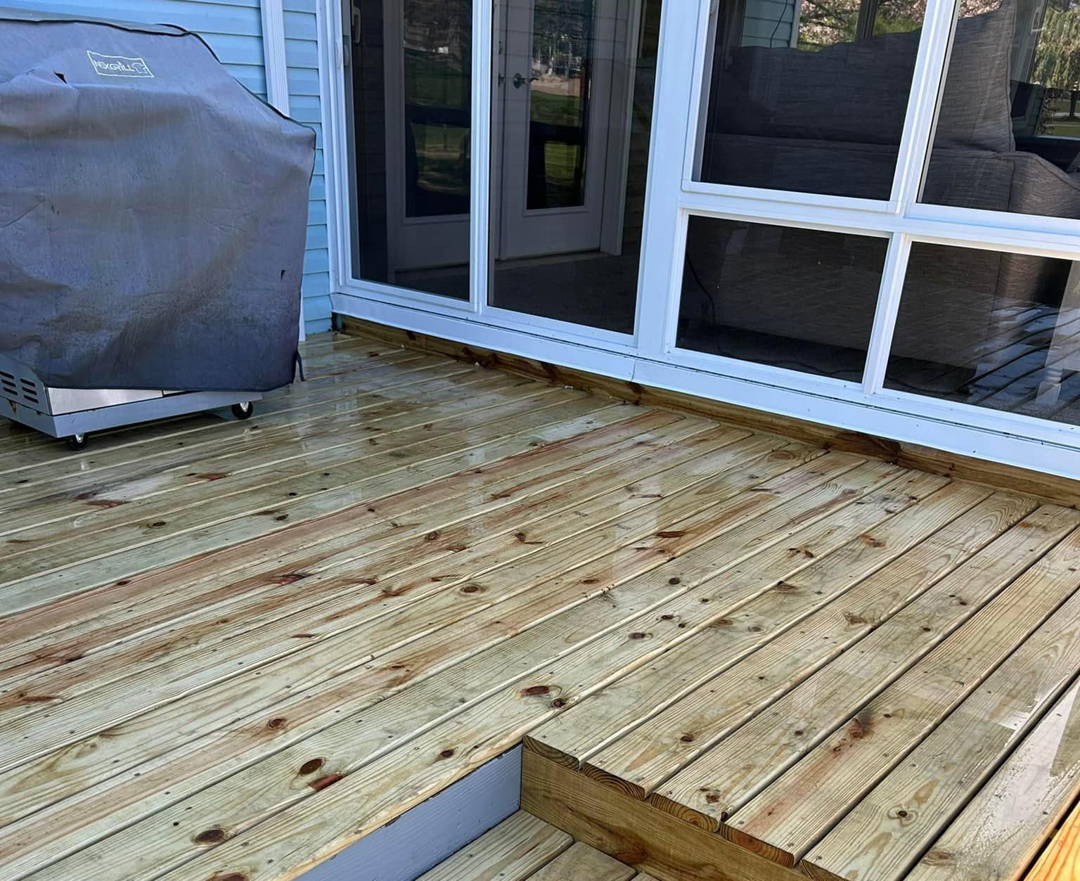 Wooden backyard deck with a covered grill beside sliding glass doors