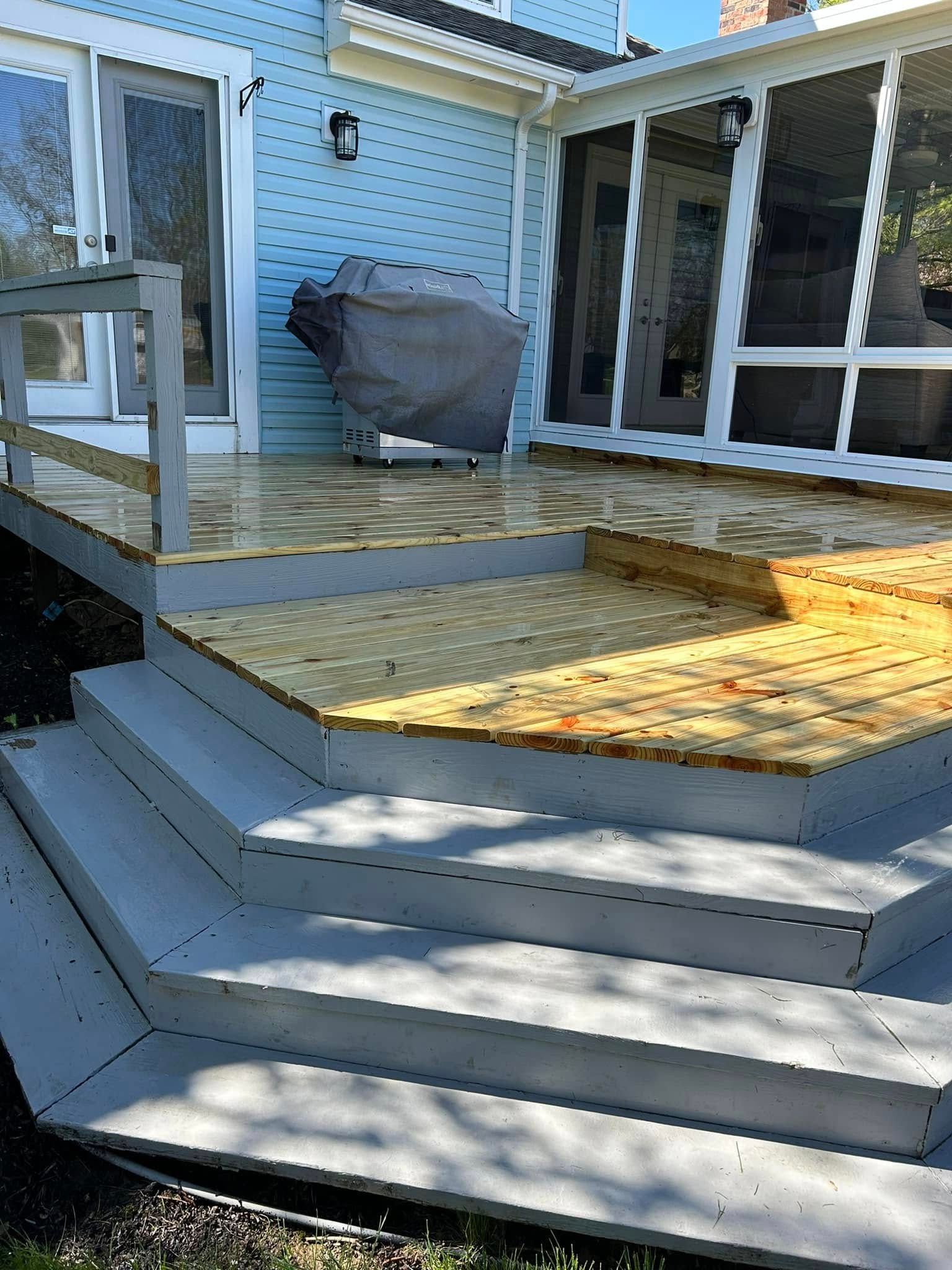 Back deck with gray steps, wooden ramp, and patio furniture beside a house