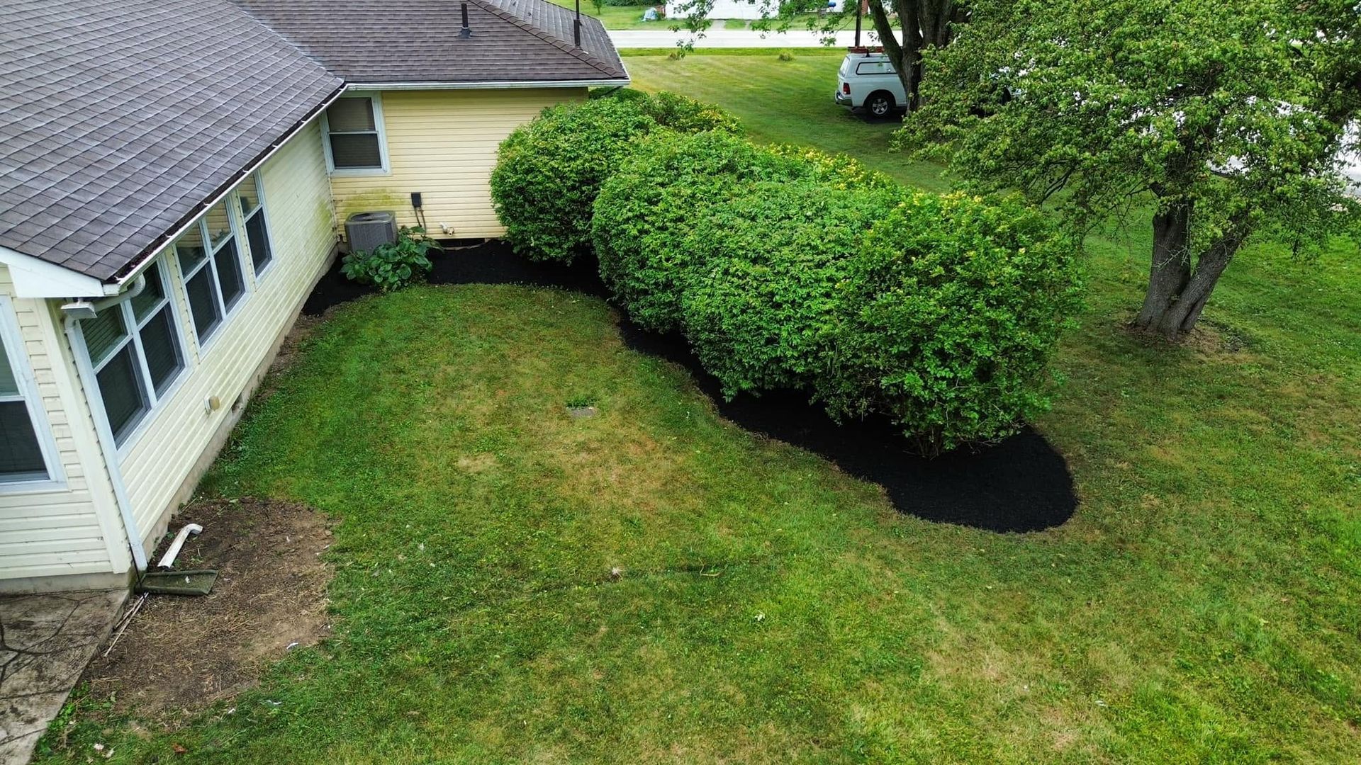 Aerial view of a house with a green lawn, dense hedge, and a small pond near a tree.