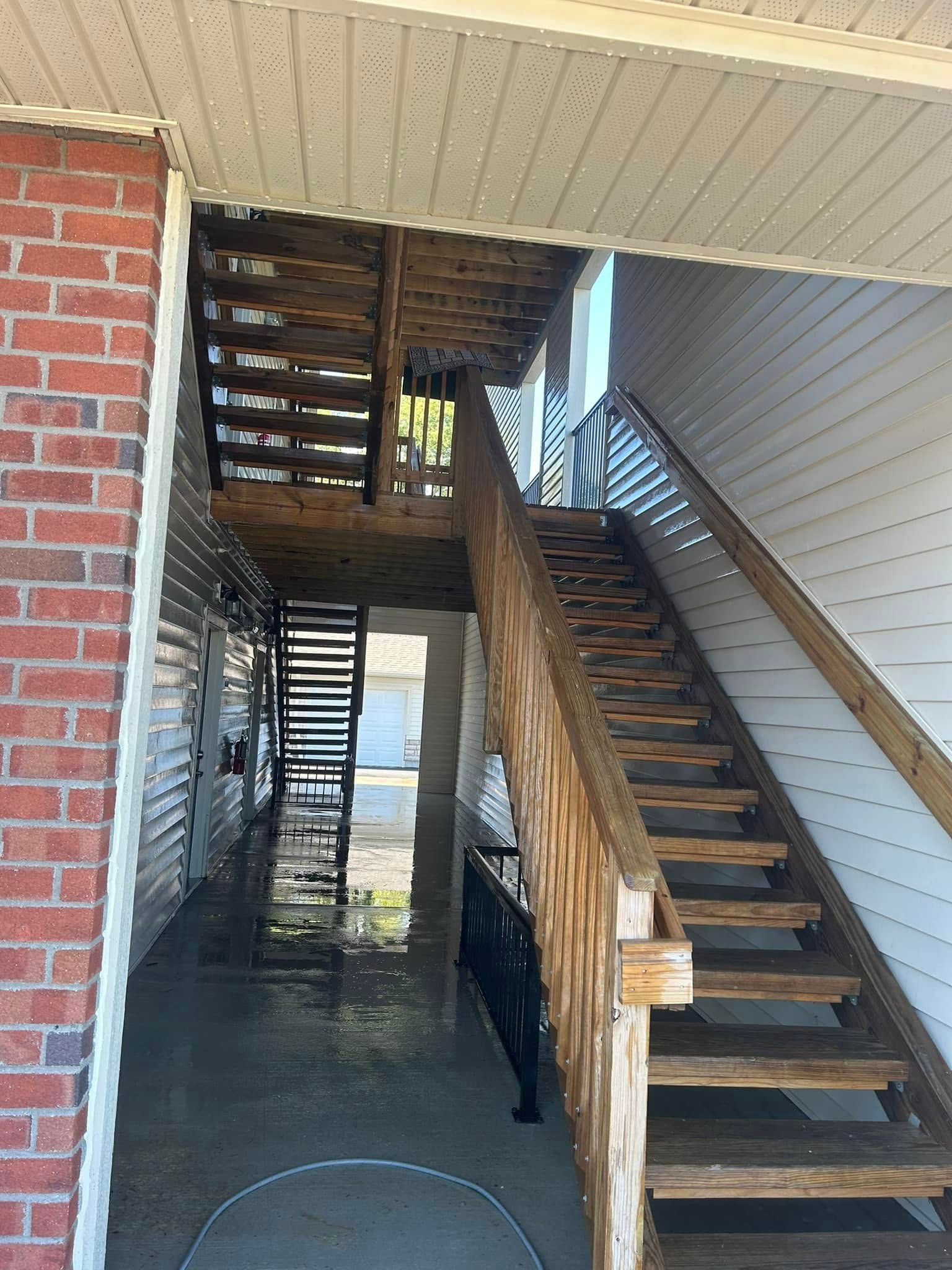 Covered outdoor stairwell with wooden stairs and railings beside a brick wall and white siding.