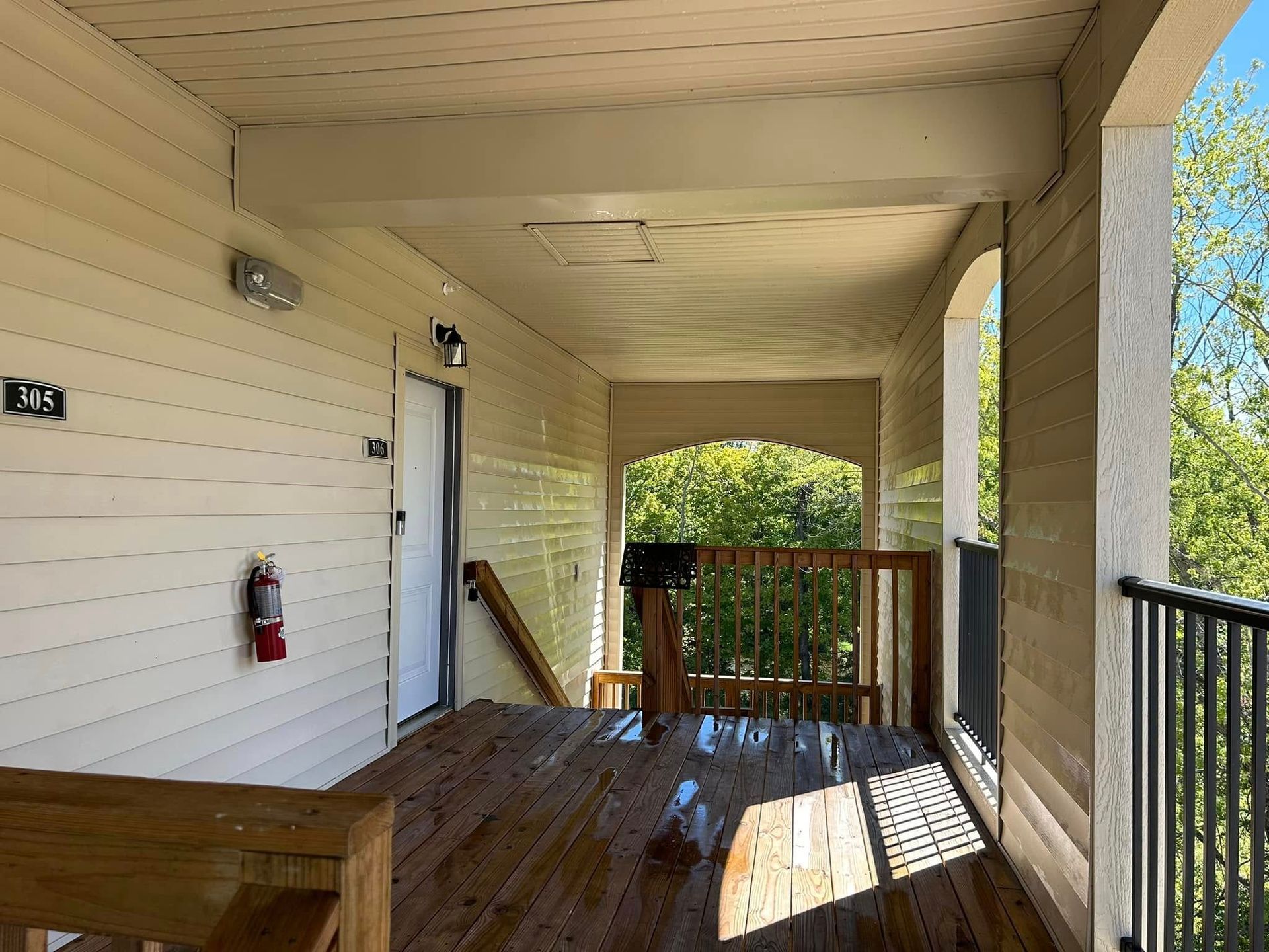 Covered wooden porch with white siding, railings, and sunlight streaming through openings