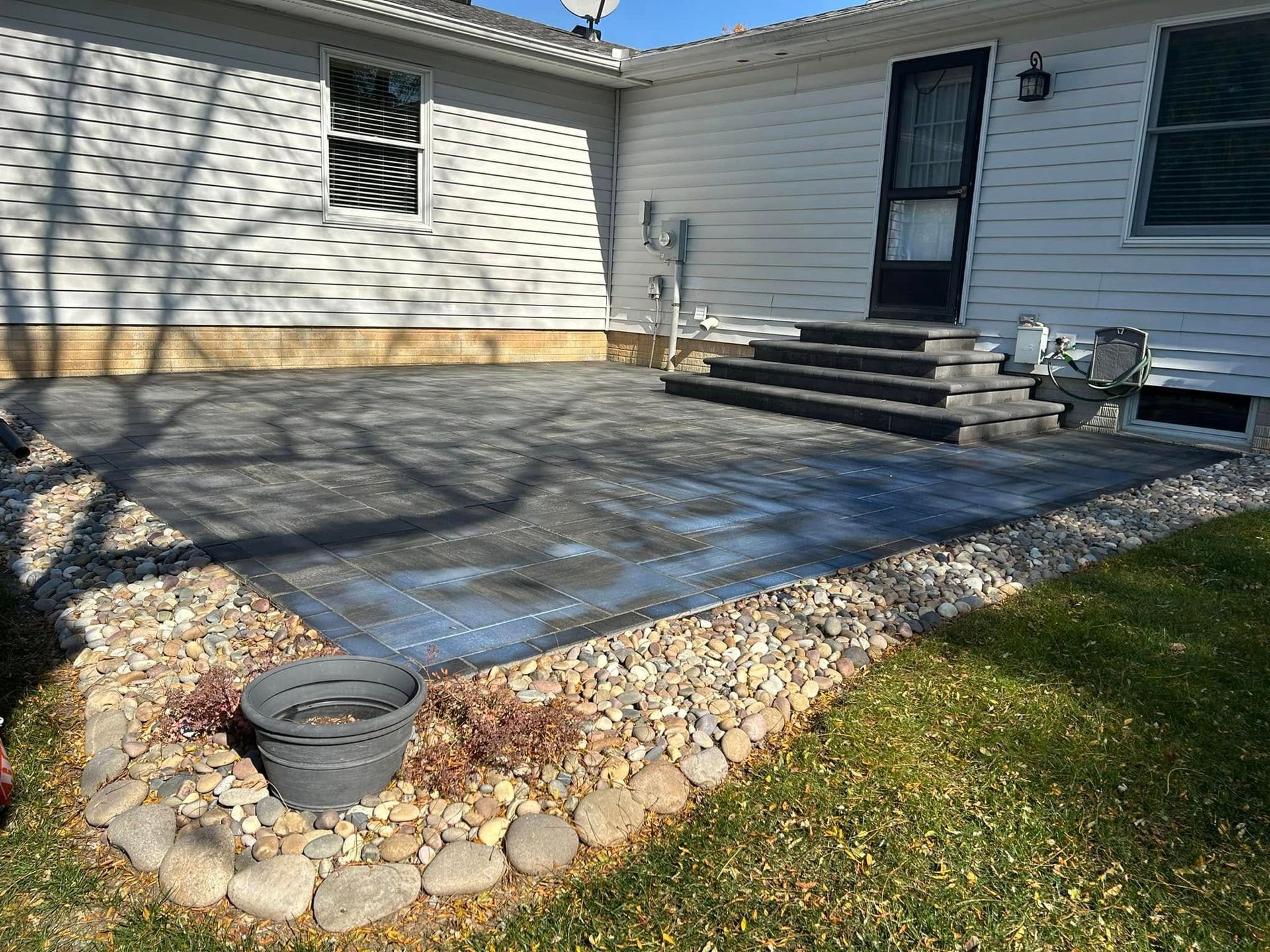Backyard patio with stone pavers, steps to a white house, and a garden border of rocks and grass