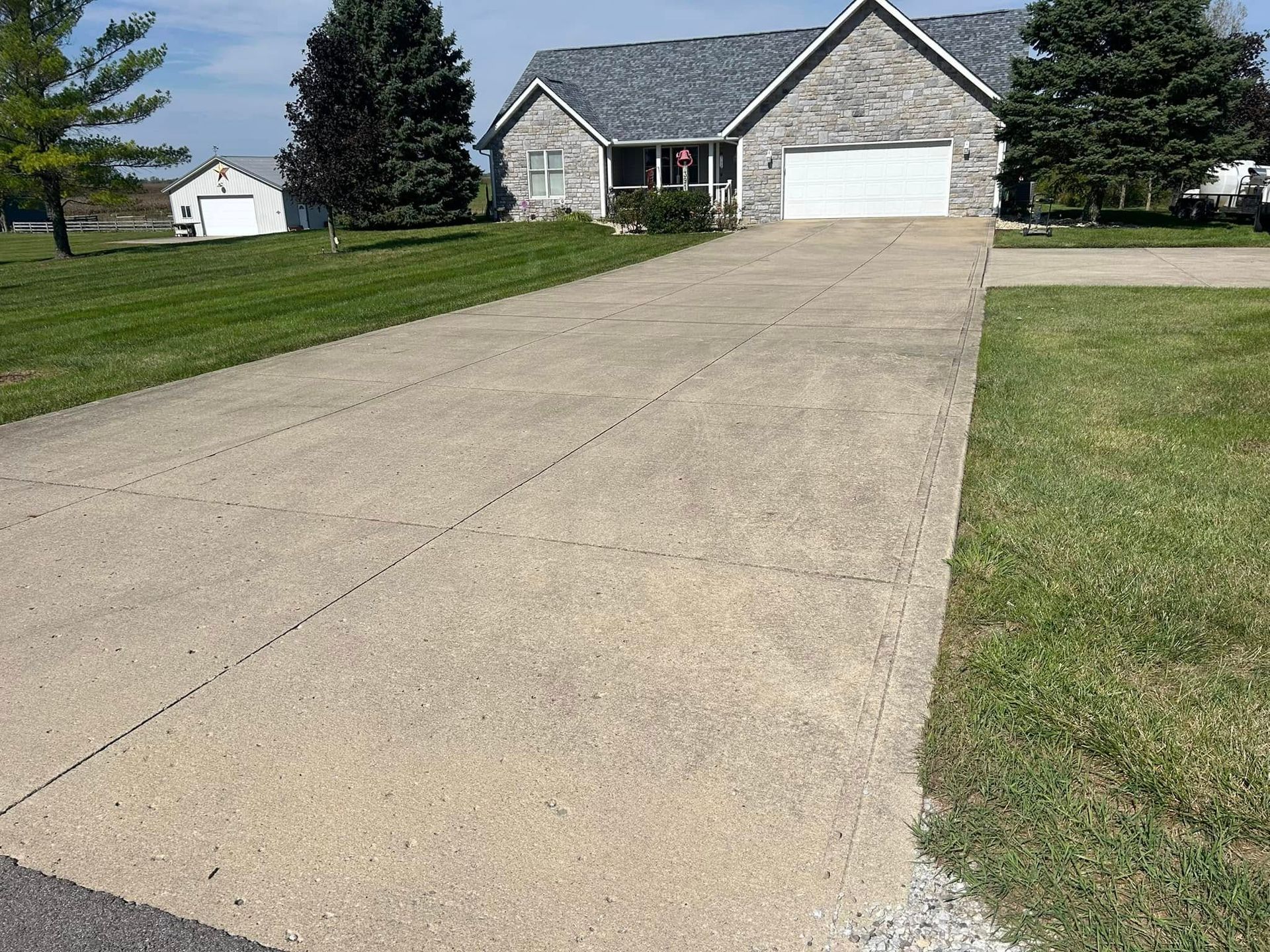 Long concrete driveway leading to a stone house with a white garage door on a grassy suburban lot