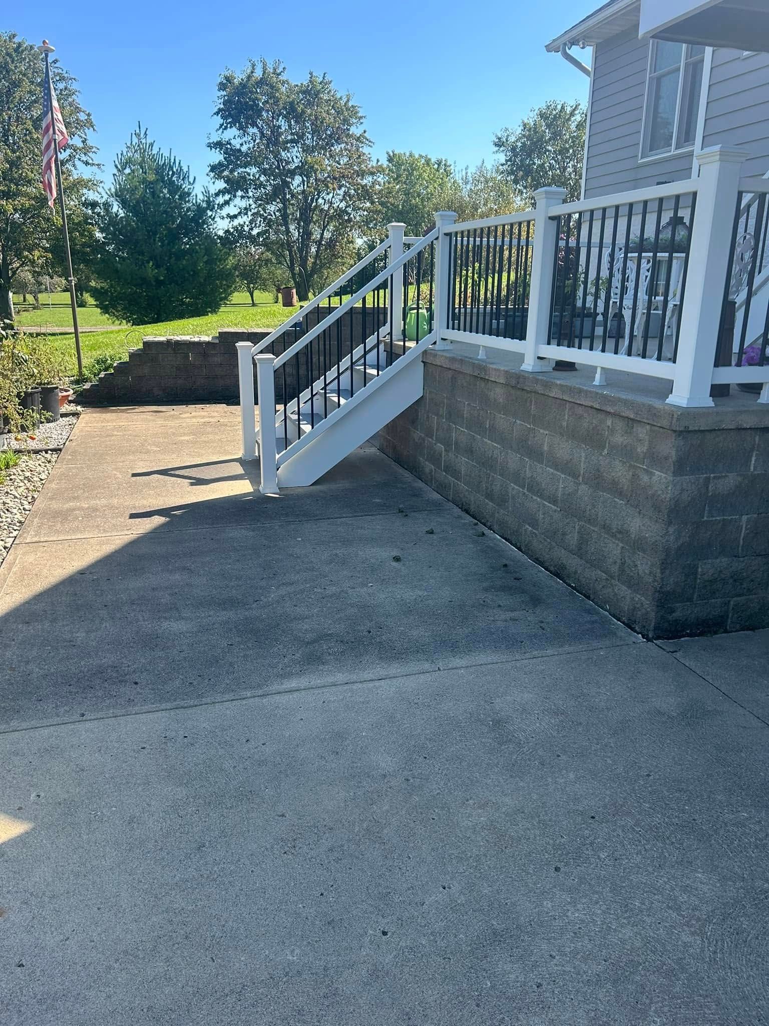 White porch steps with railing beside a house, leading to a paved driveway and green yard under blue sky
