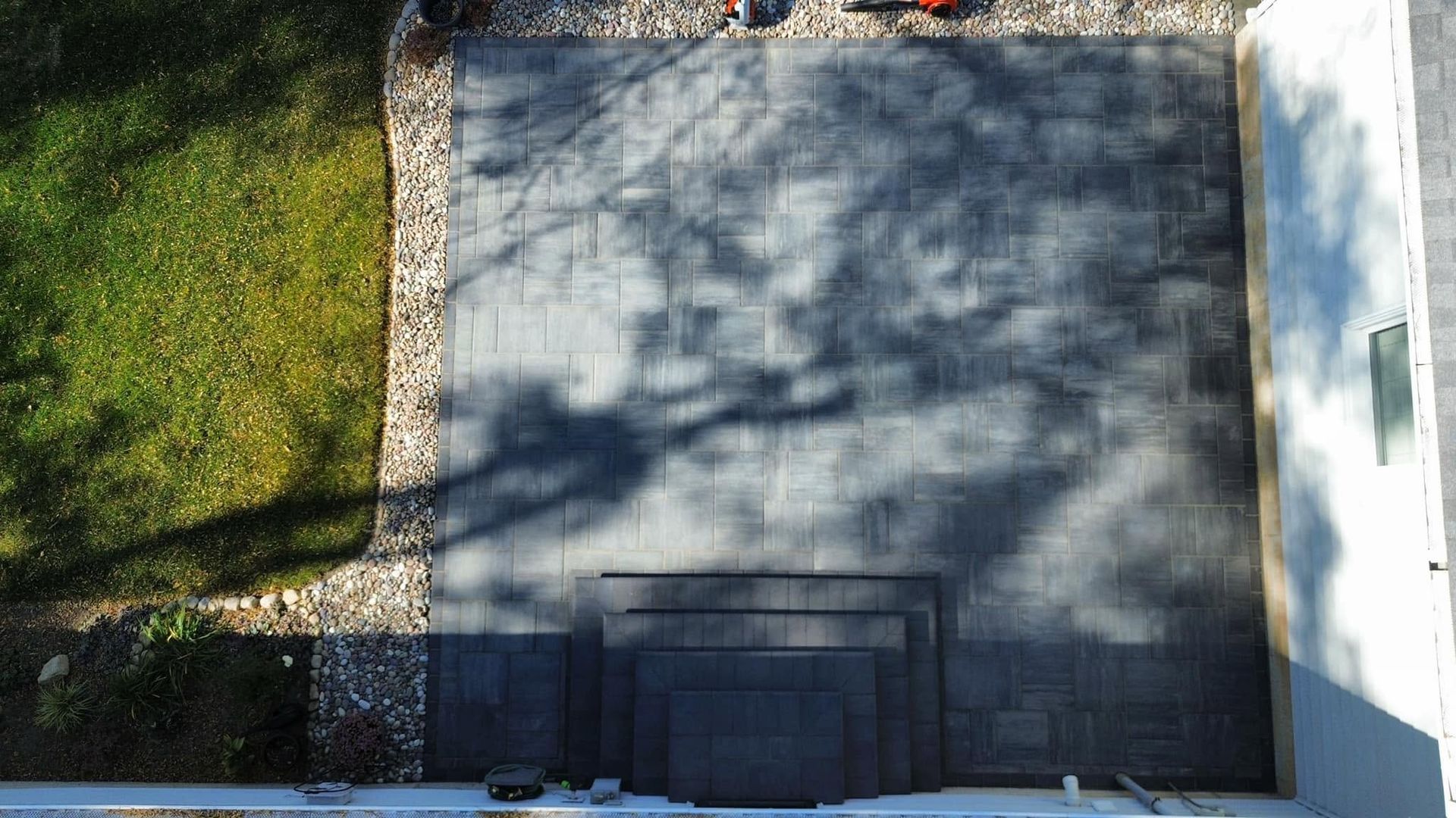 Aerial view of a driveway beside a grassy yard and white house, with shadows across the pavement.