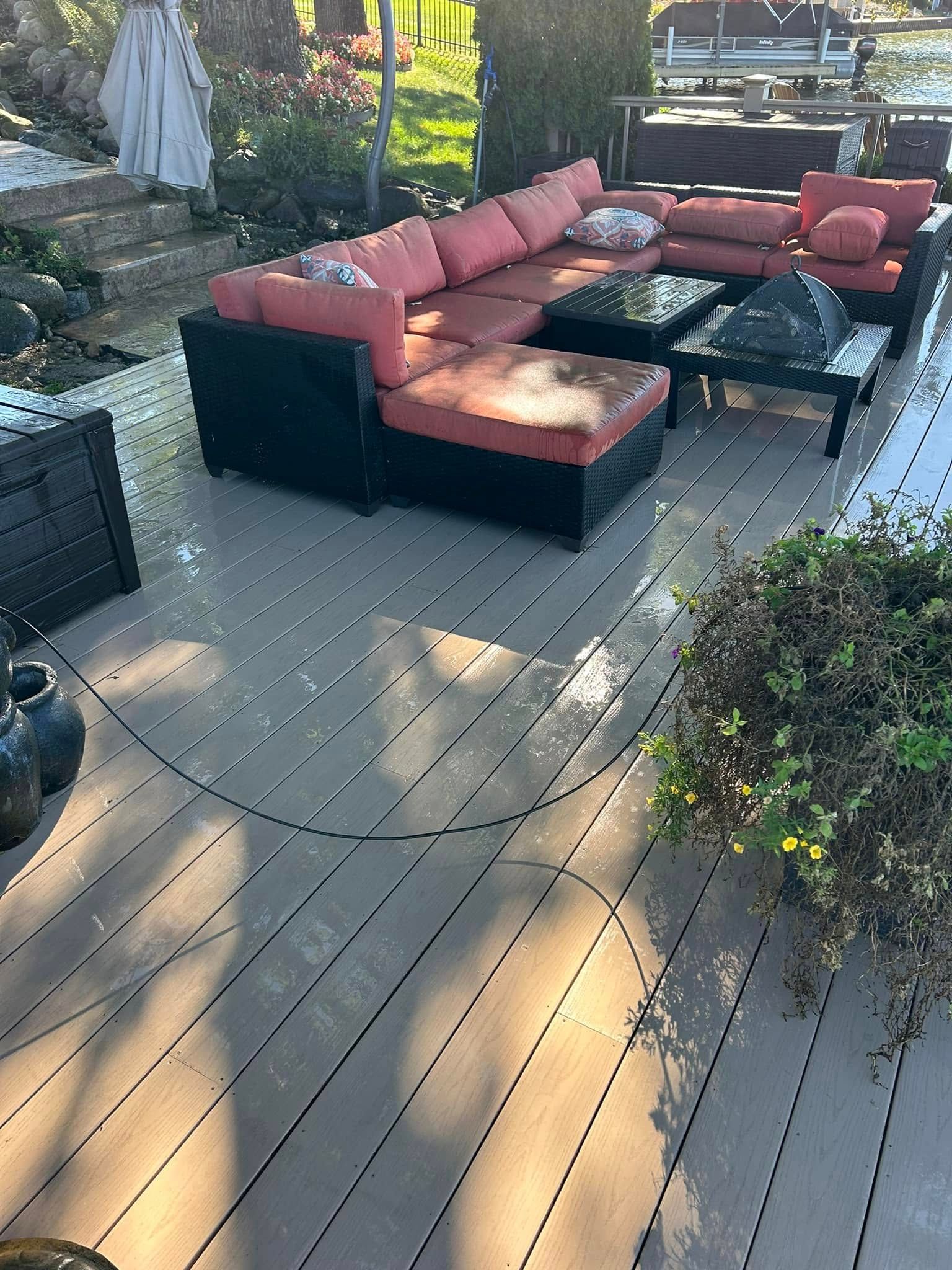 Outdoor patio with black sectional sofa, red cushions, and glass coffee table on a gray deck