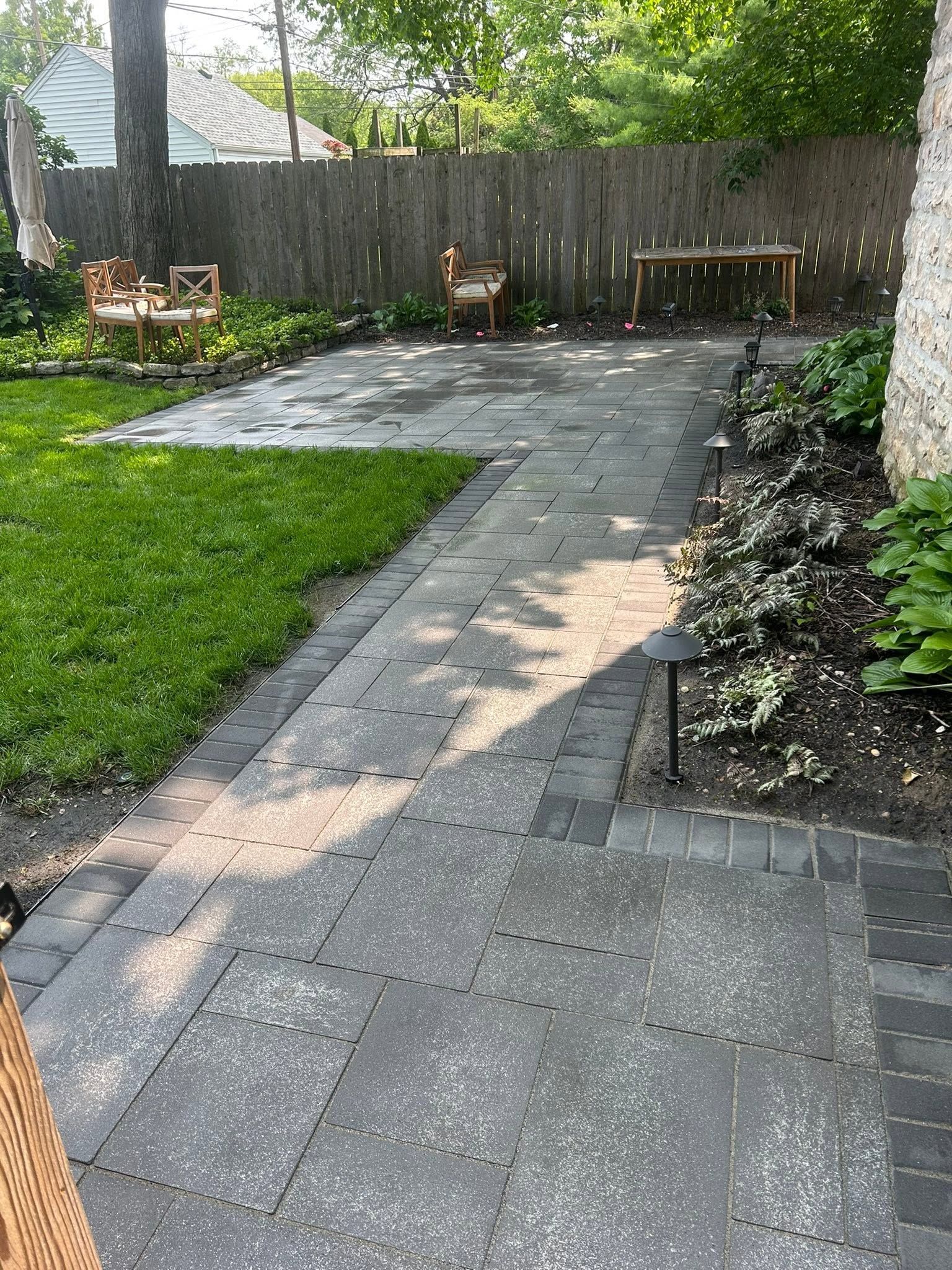 Backyard patio with gray stone walkway, green lawn, and wooden fence in sunlight