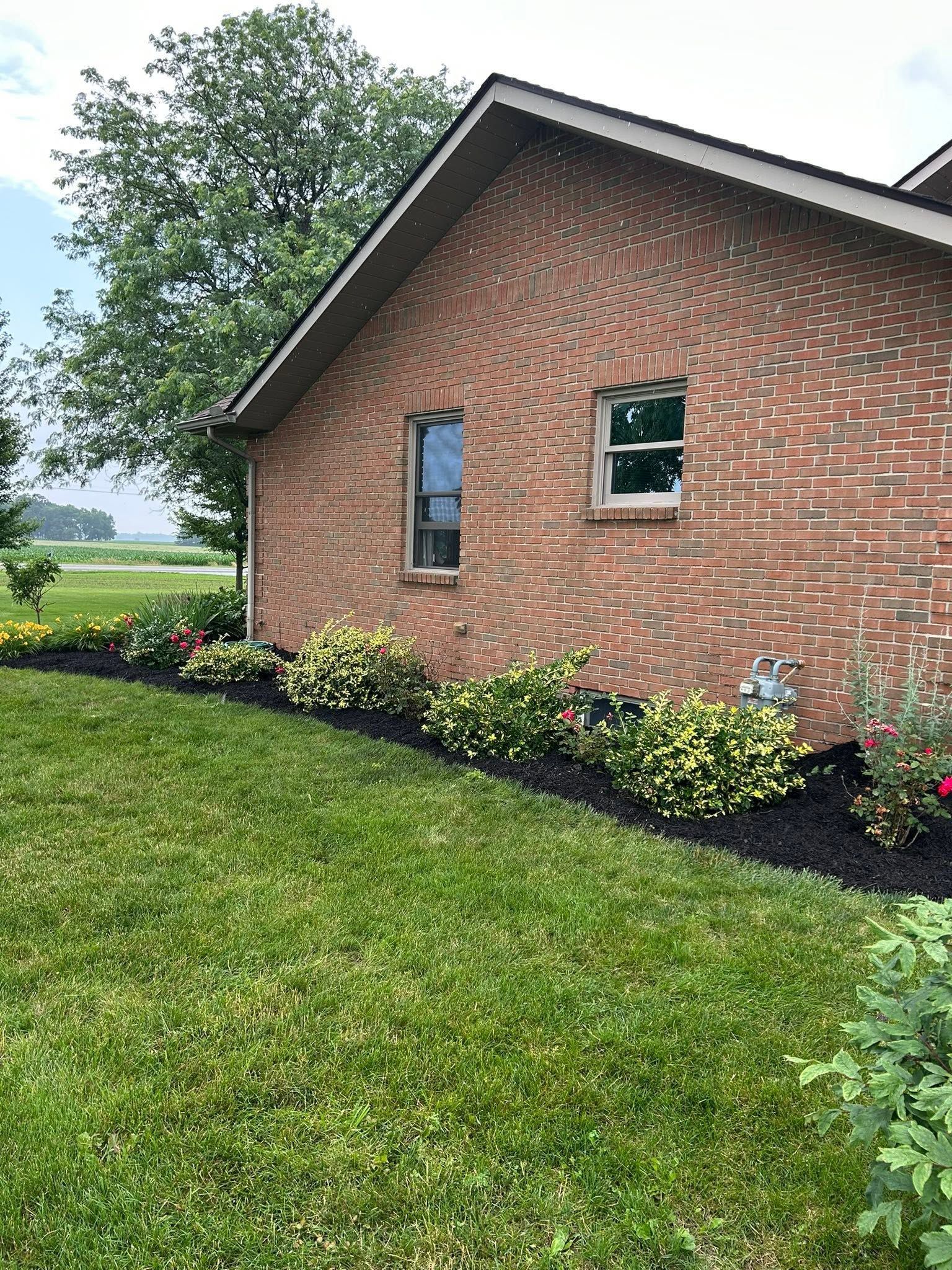 Brick house with green lawn and landscaped flower bed under cloudy sky