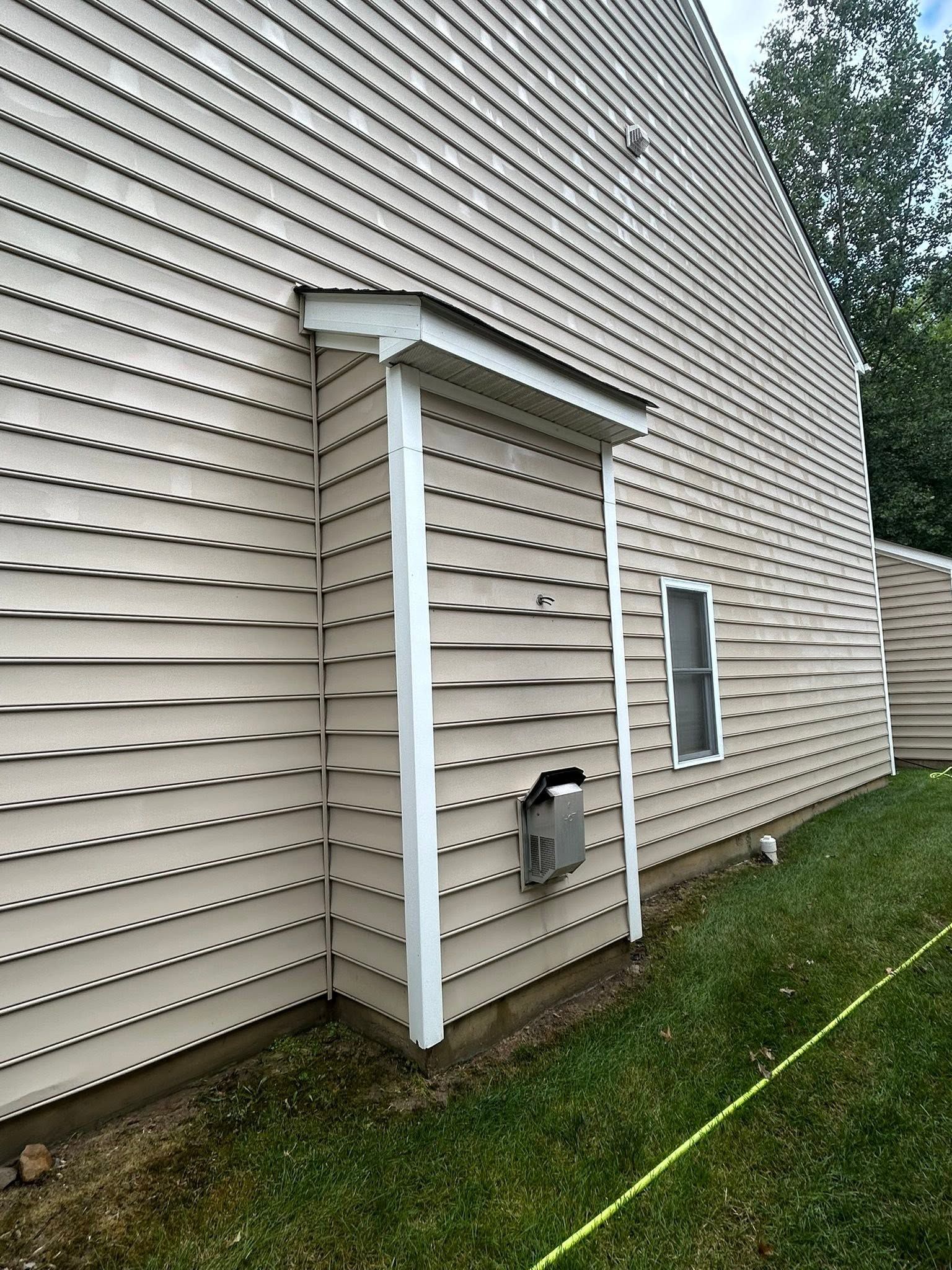 Exterior house siding with white utility supports and a small window on the side wall