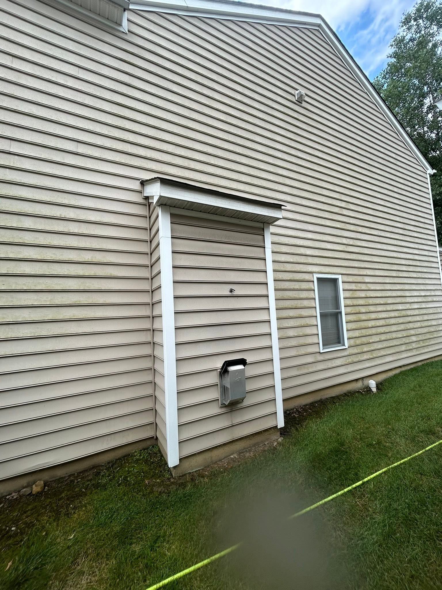 Side view of a beige vinyl-sided house with a small covered entrance and grassy yard.